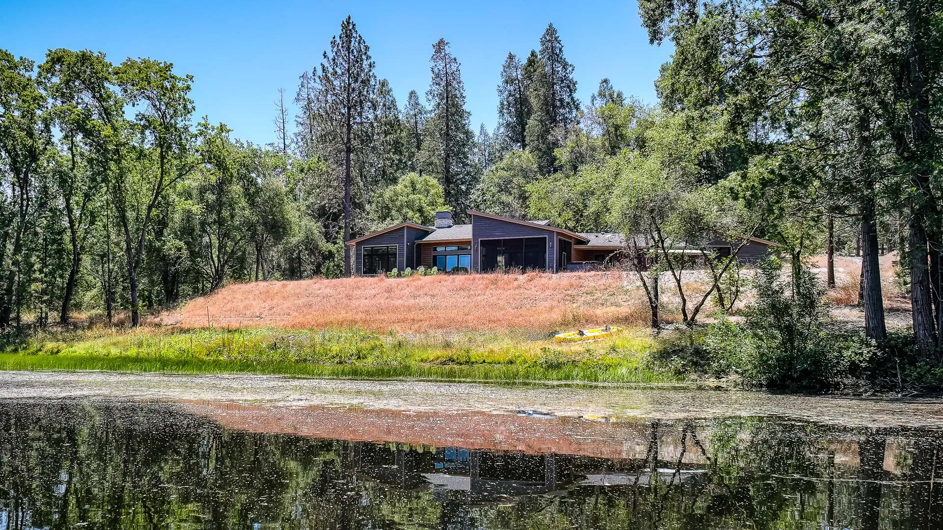 View across the pond to the modern retreat on its grassy hillside, kayak resting on the bank