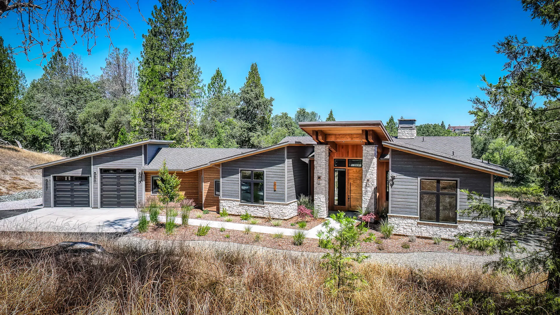 Timber-and-stone entry portico of this custom home in Somerset, California, framed by drought-tolerant landscaping