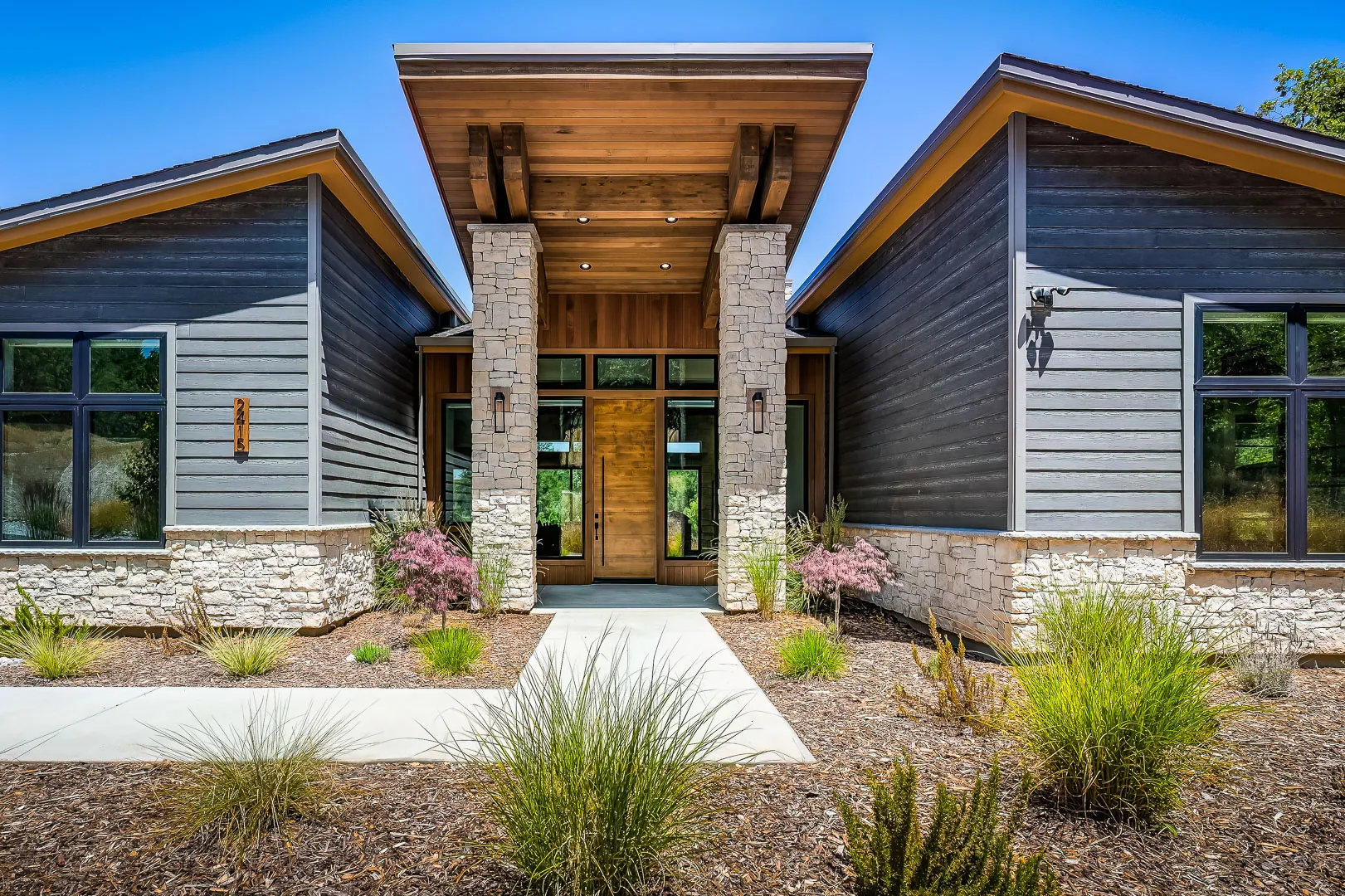 Entry courtyard with stacked-stone columns, cedar-wrapped portico, and a plank wood front door