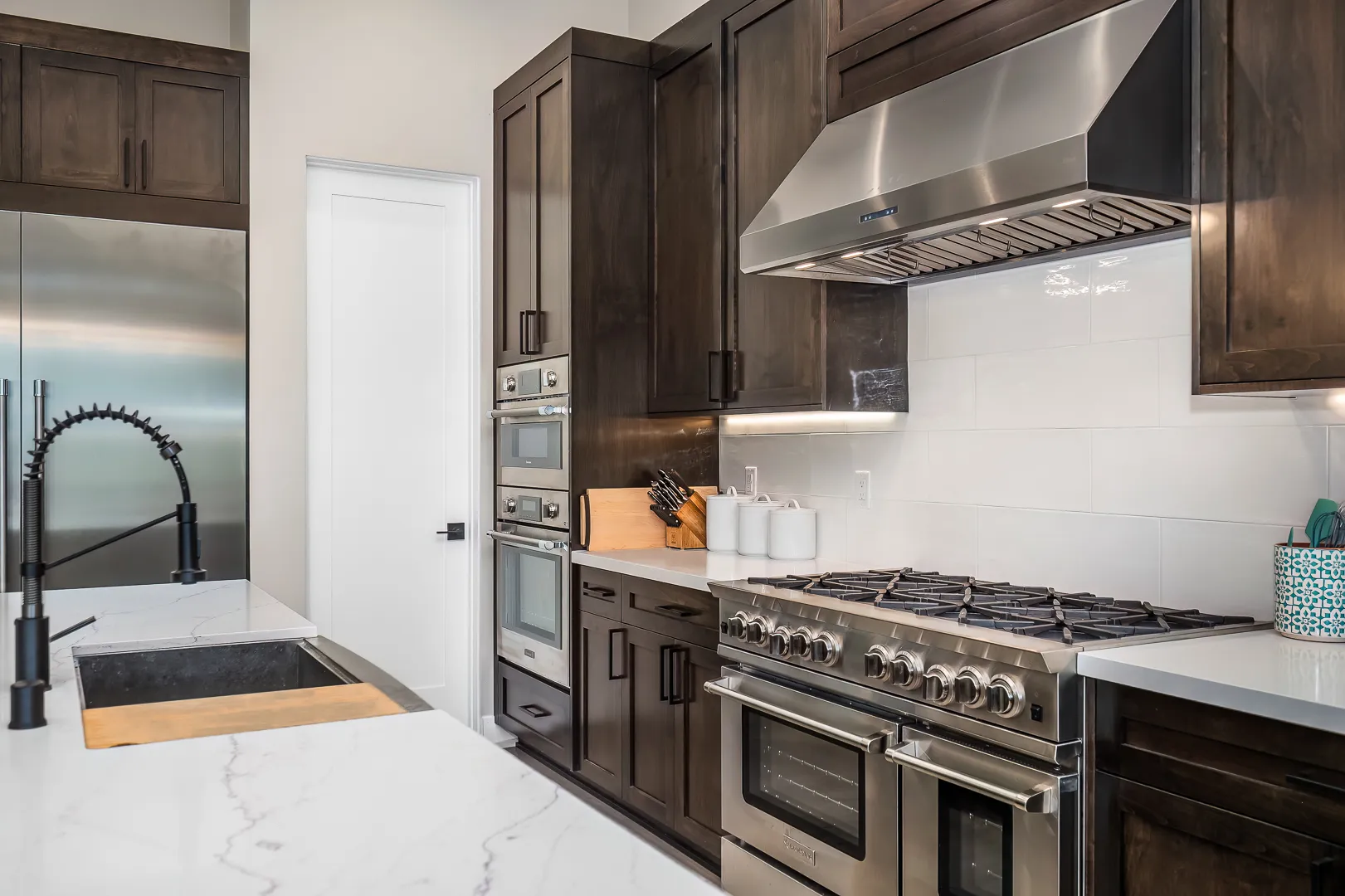 Professional stainless range and hood flanked by dark wood cabinetry and marble-look quartz counters