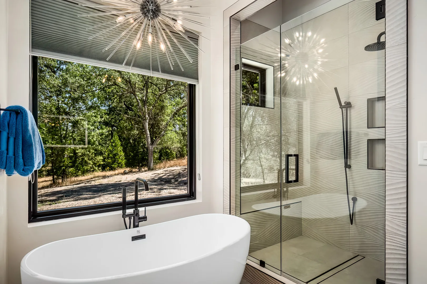 Freestanding soaking tub under a picture window beside a glass shower with sculpted wave tile