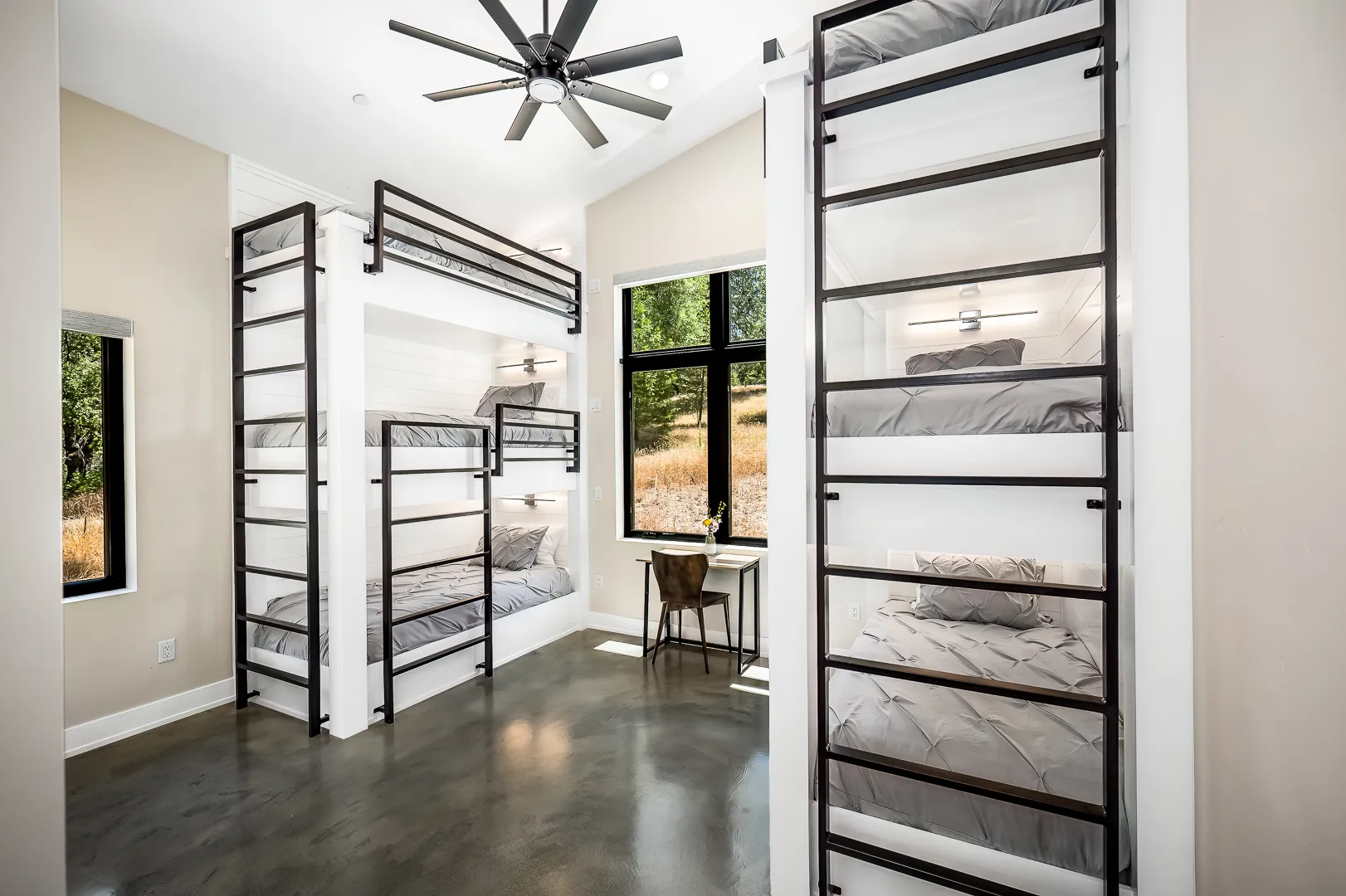 Bunk room with six built-in bunks, black steel ladders, reading lights, and a study desk