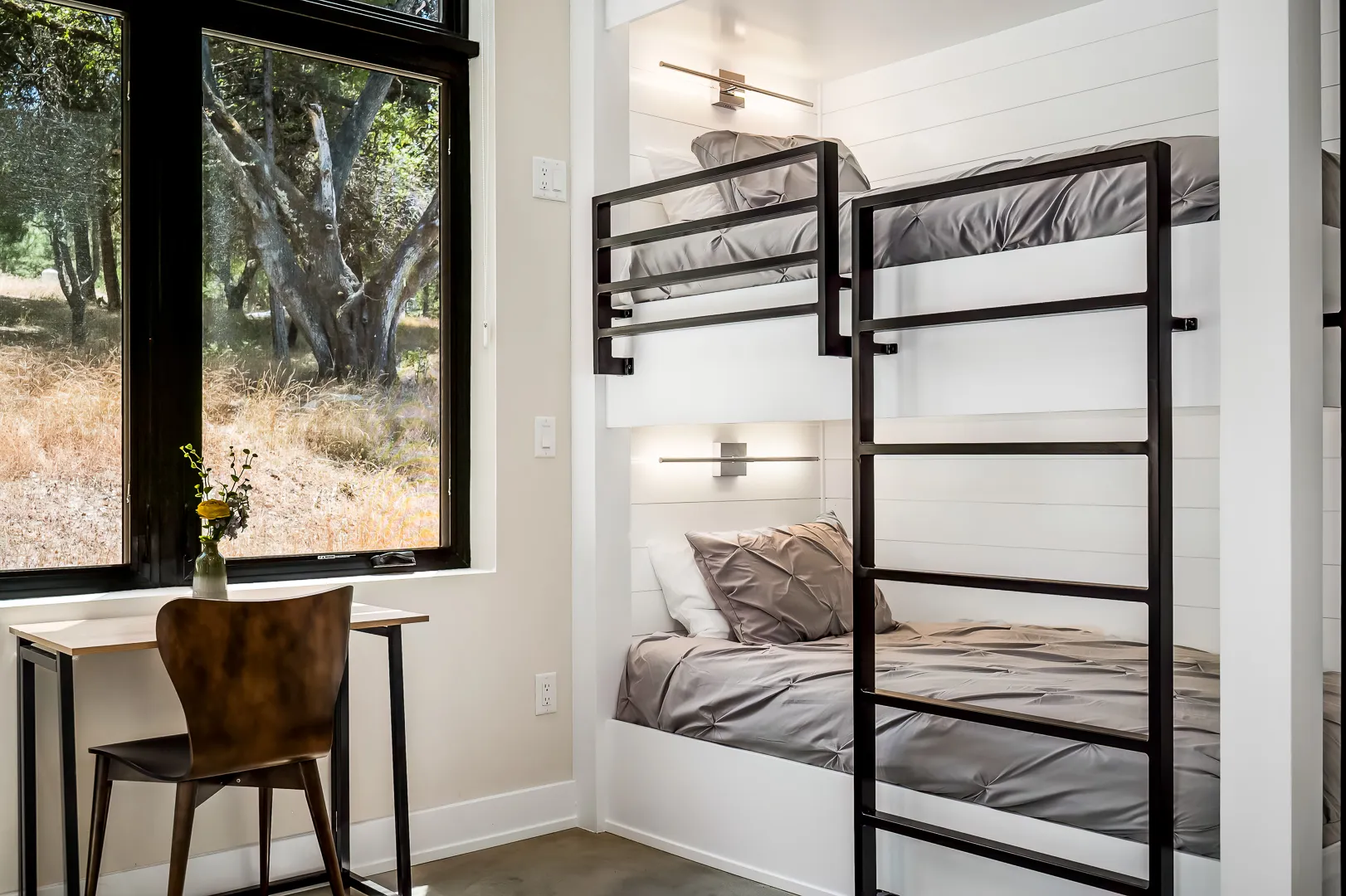 Built-in bunk beds with shiplap surrounds and sconces beside a desk at the window