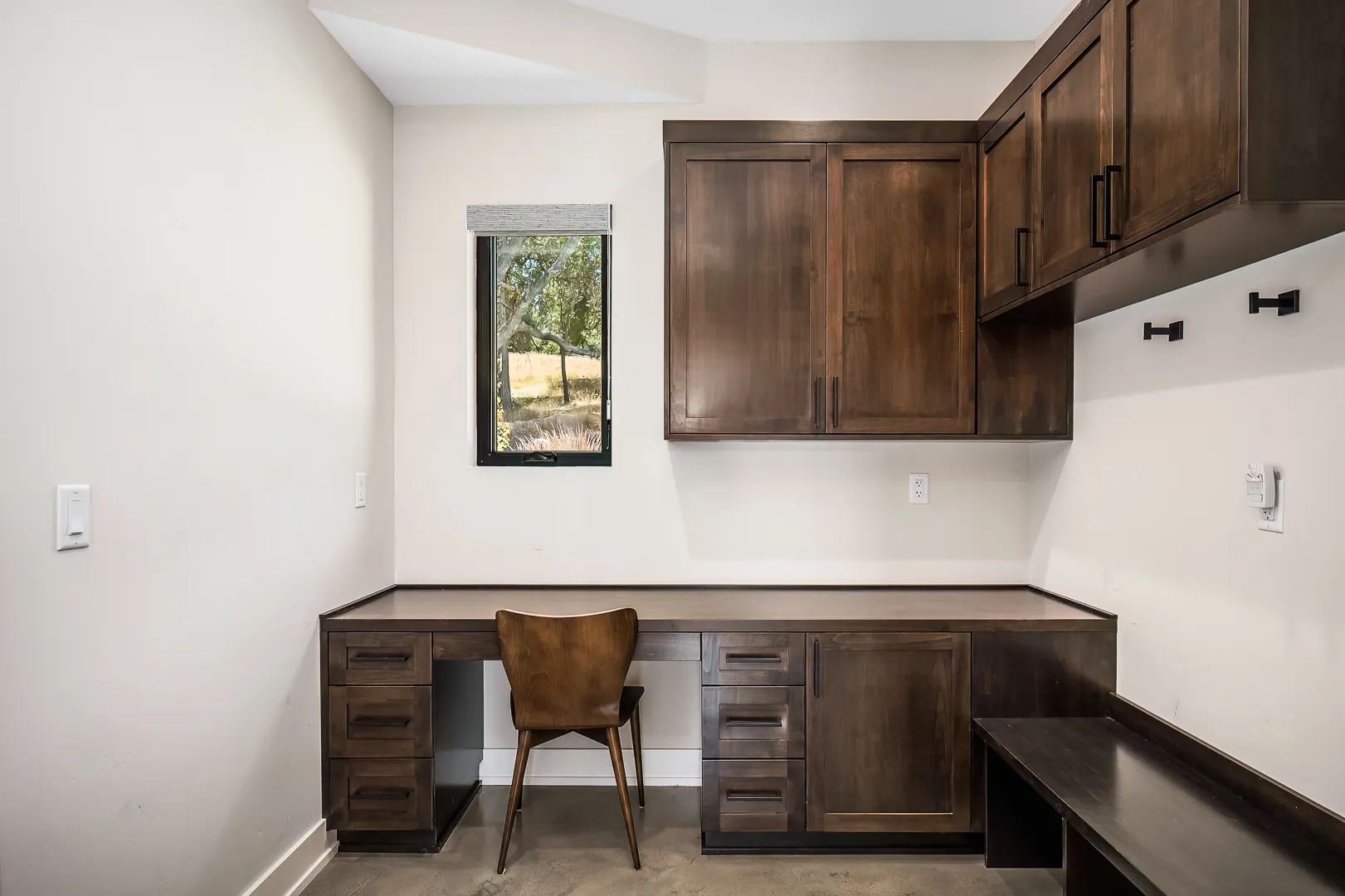 Home office nook with built-in desk, dark alder cabinetry, and a bench with coat hooks