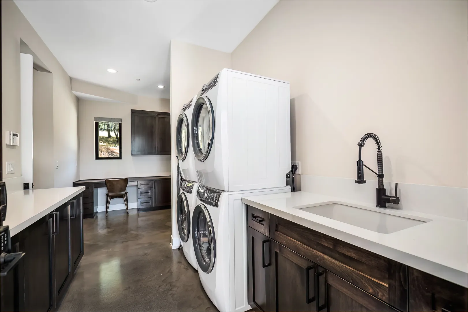Large laundry room with two stacked washer-dryer pairs, deep sink, and quartz folding counters