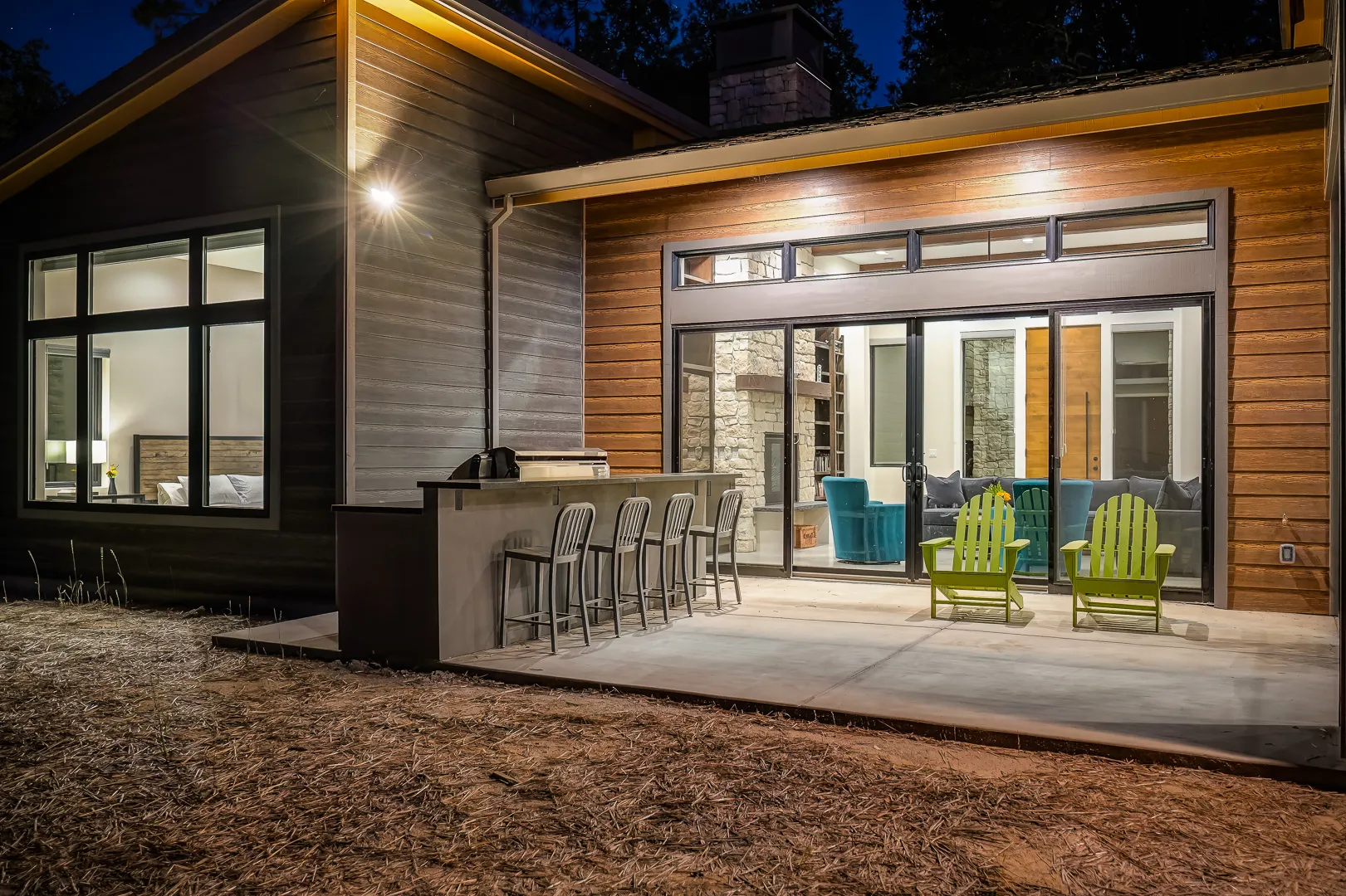 Rear patio at night with bar seating, warm interior light spilling from the great room