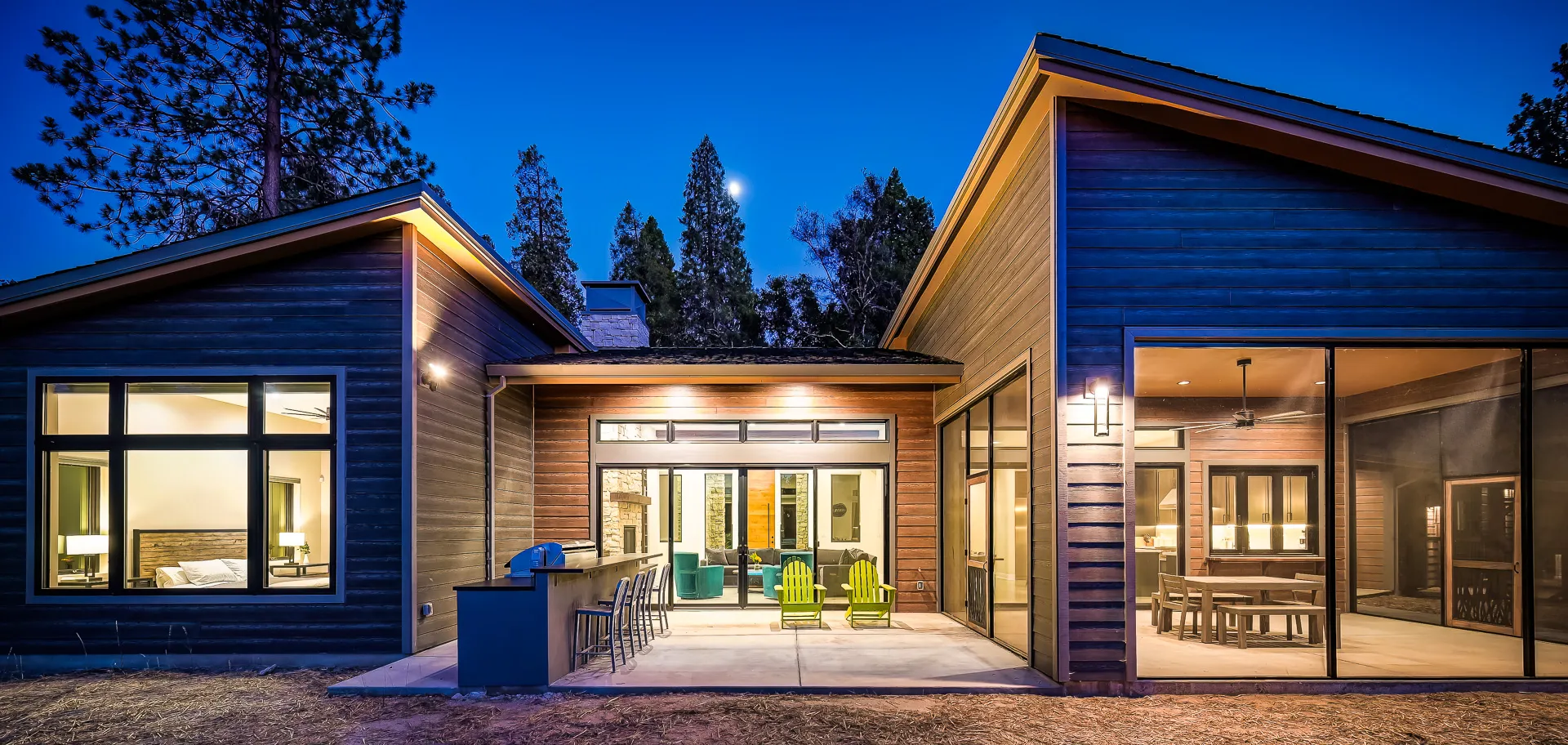 Moonlit rear elevation with lit outdoor kitchen, screened dining porch, and bedroom windows aglow