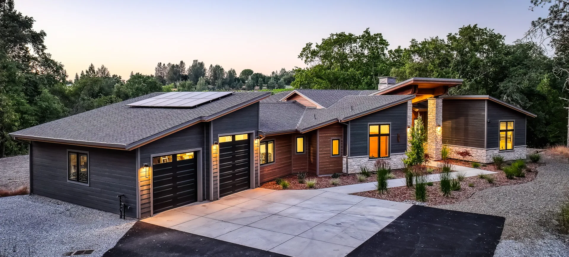 Twilight aerial of this custom home in Somerset, California, with solar roof and lit three-car garage