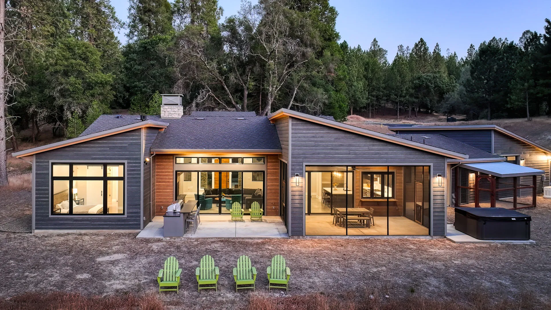Rear elevation at dusk with four green Adirondack chairs in the meadow facing the house