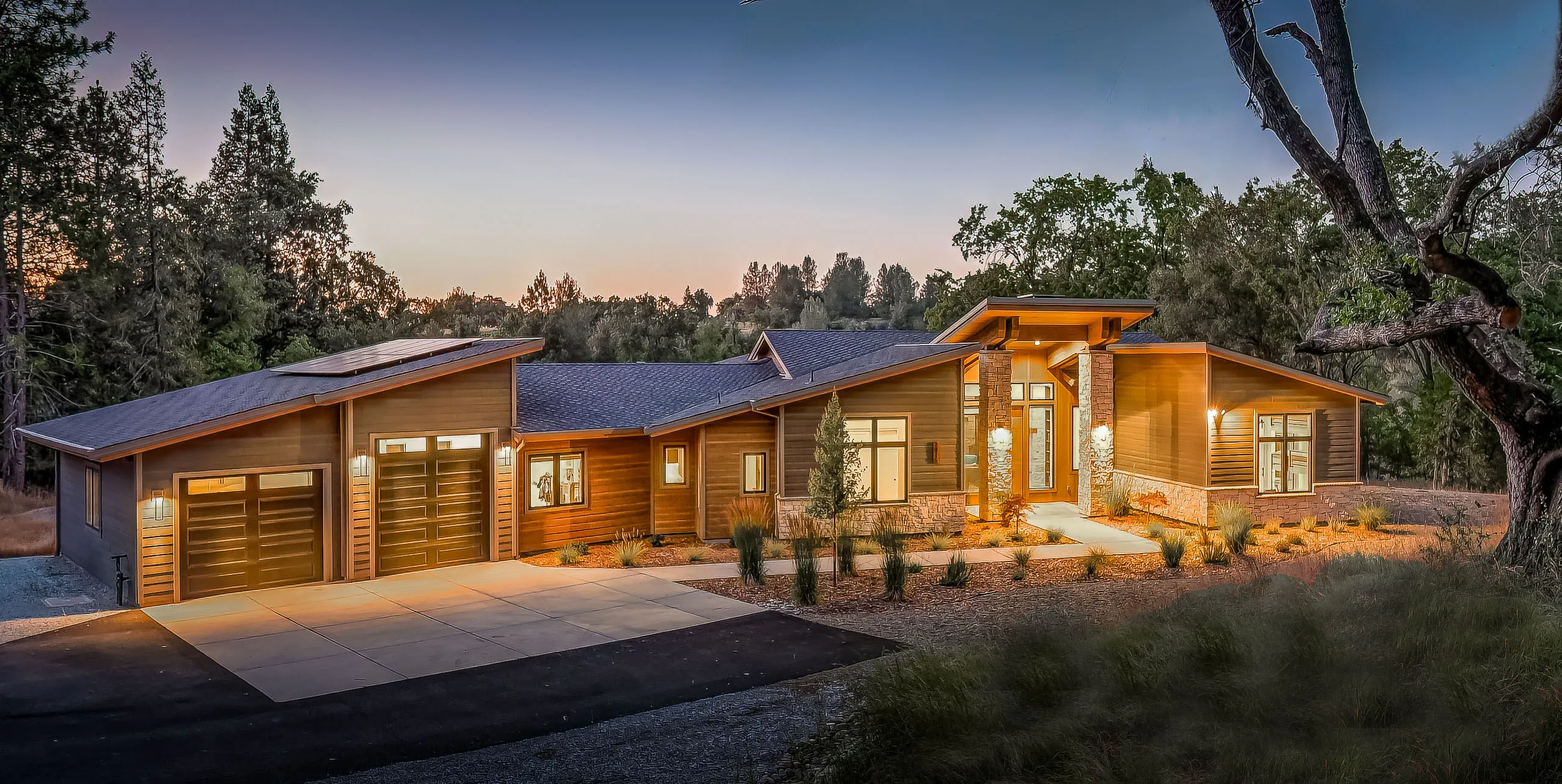 Front exterior at dusk, garage doors and entry portico glowing with warm landscape lighting