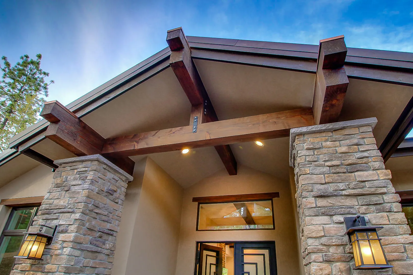 Entry portico detail with exposed timber trusses, stacked-stone columns, and craftsman lantern sconces