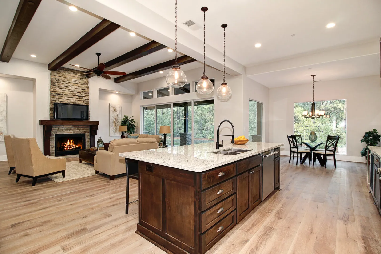 Open great room with dark beamed ceiling, stacked-stone fireplace, and granite-topped kitchen island