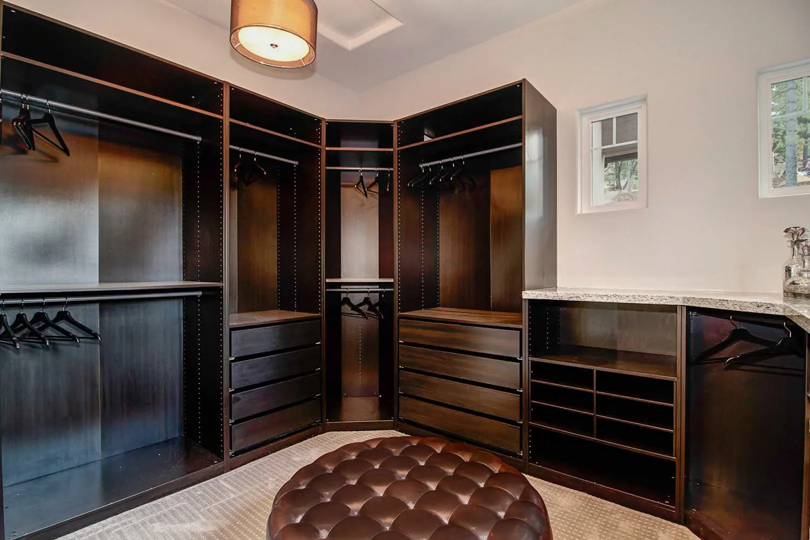 Walk-in closet with dark wood built-ins, granite-topped dresser, and tufted leather ottoman