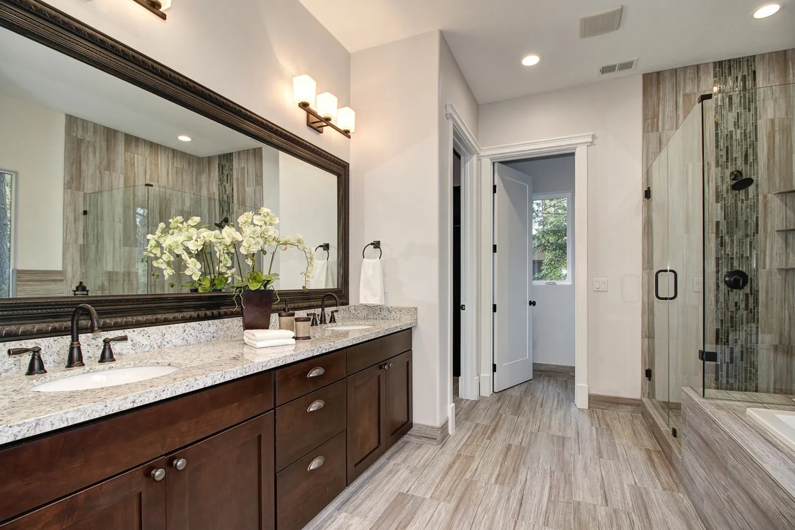 Primary bath with dual-sink granite vanity, framed mirror, and glass-enclosed tile shower