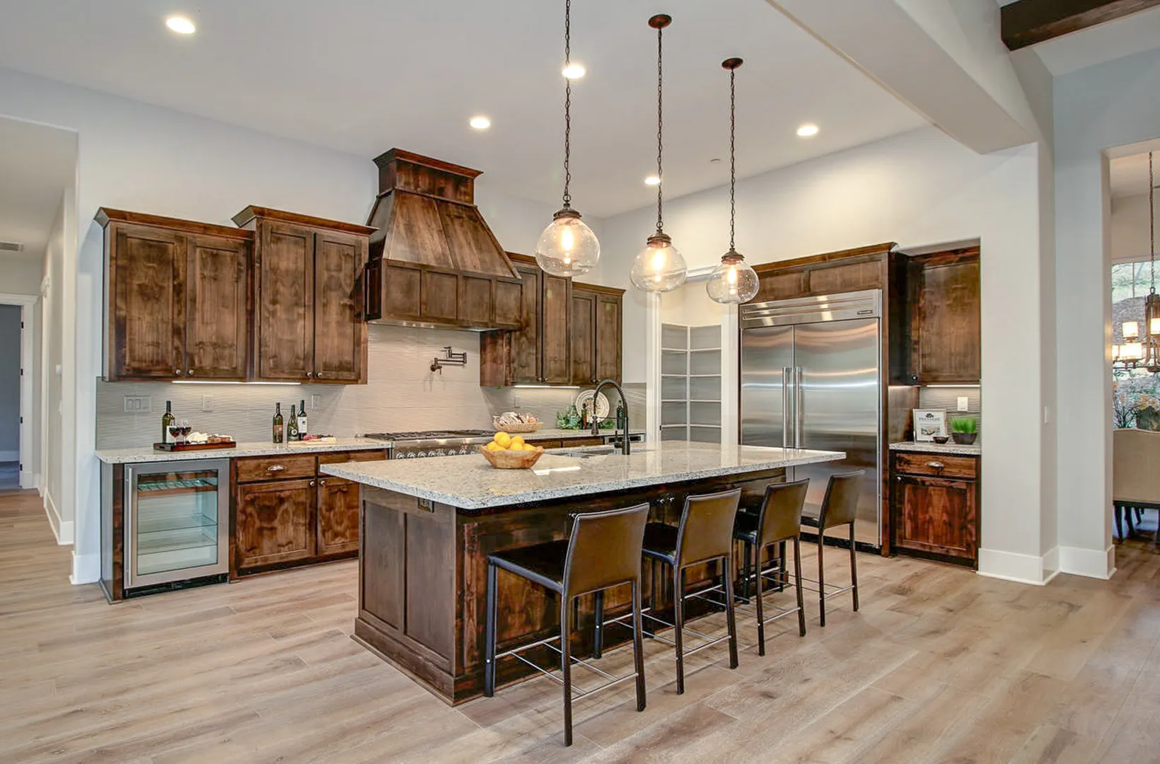 Kitchen with knotty alder cabinetry, wood range hood, seeded-glass pendants, and stainless appliances
