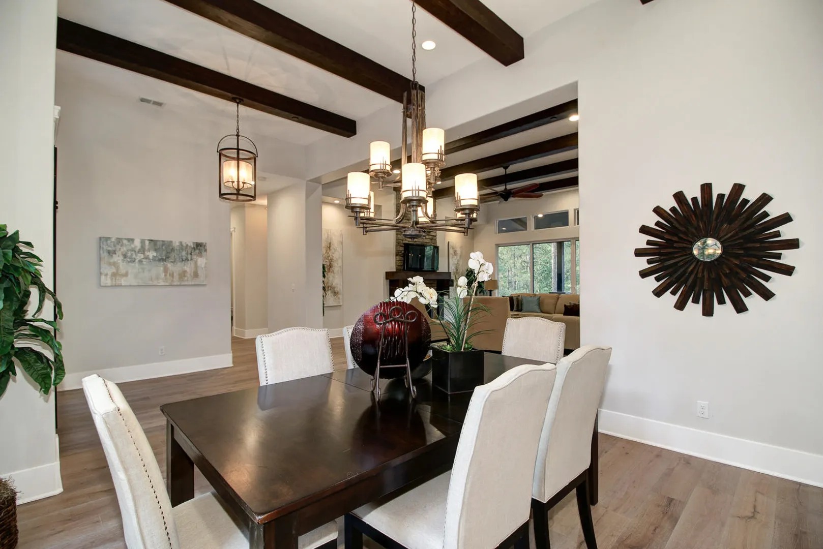 Formal dining room under dark ceiling beams with candle chandelier and sunburst wall art