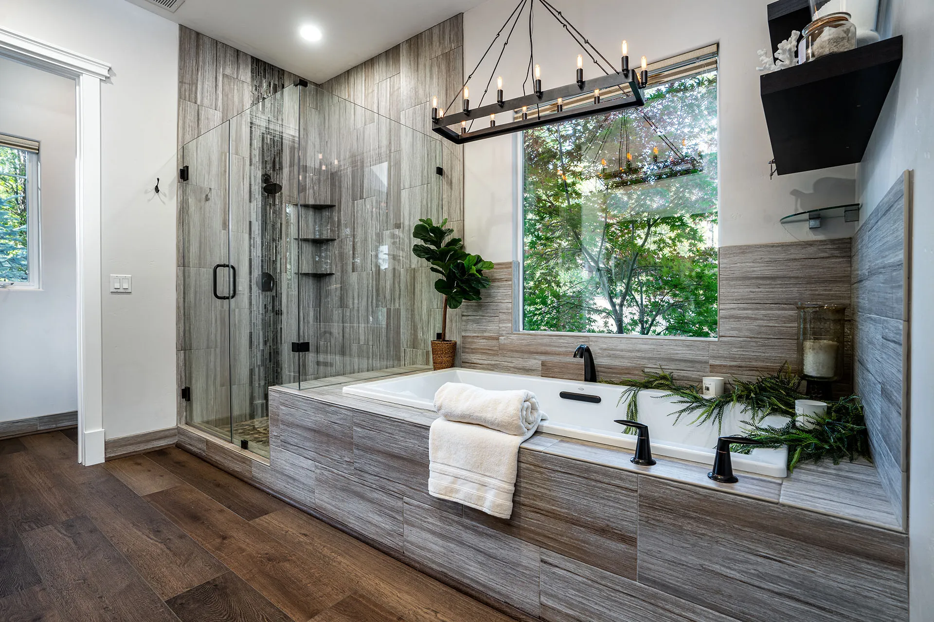 Spa-style bath with tile-clad soaking tub, garden window, and glass shower with mosaic accents