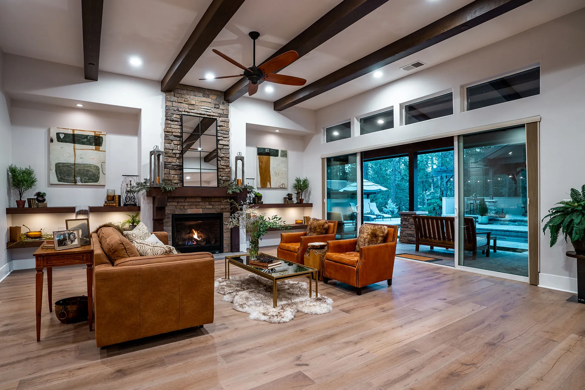 Living room with stone fireplace, leather armchairs, and sliders opening to the pool patio at dusk