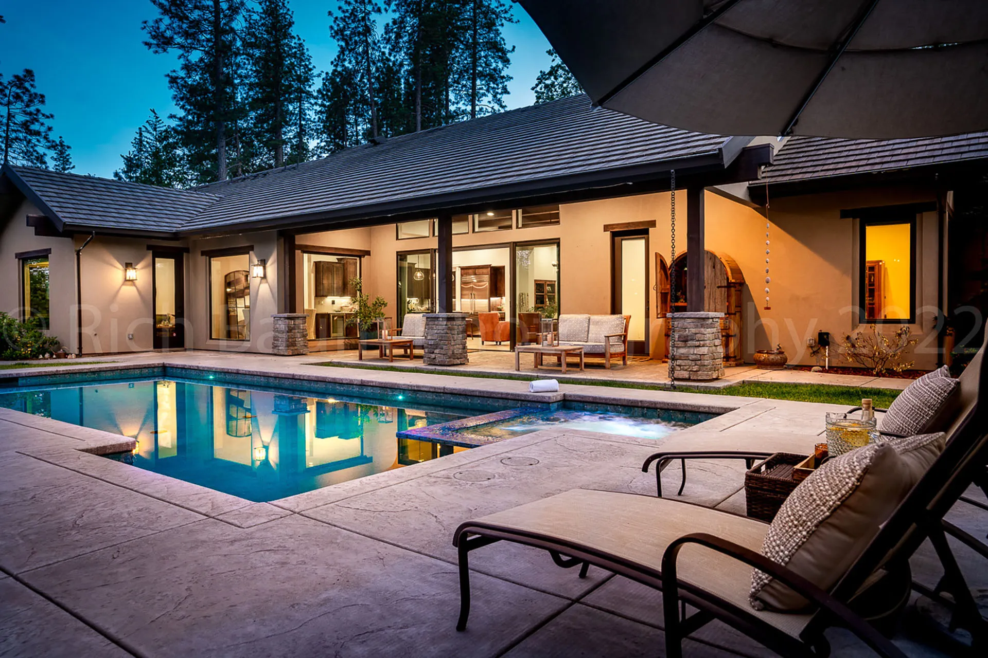 Twilight pool and spa courtyard with lounge chairs and warm light spilling from the house