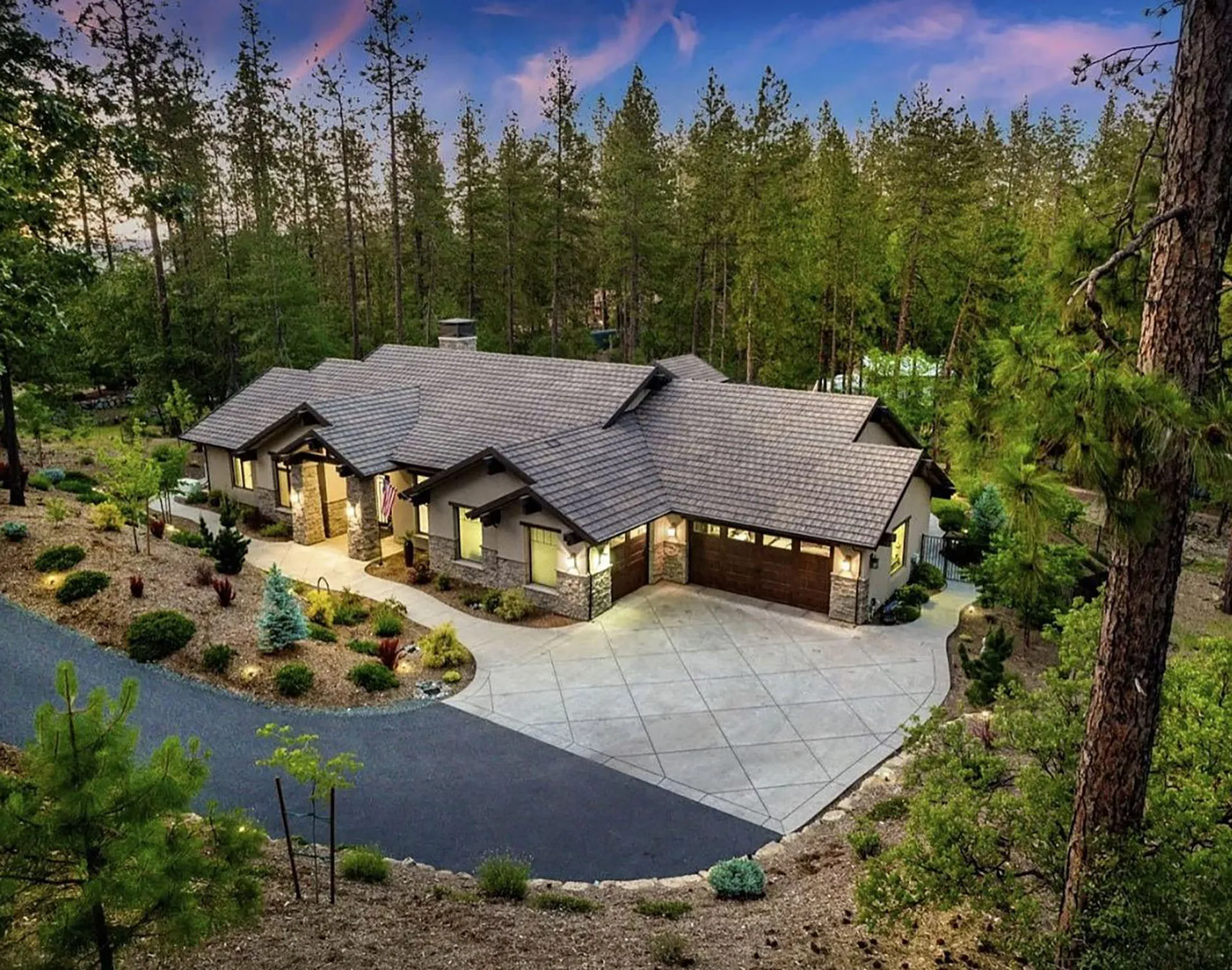 Aerial evening view of the home, curved driveway, and landscaped grounds ringed by tall pines