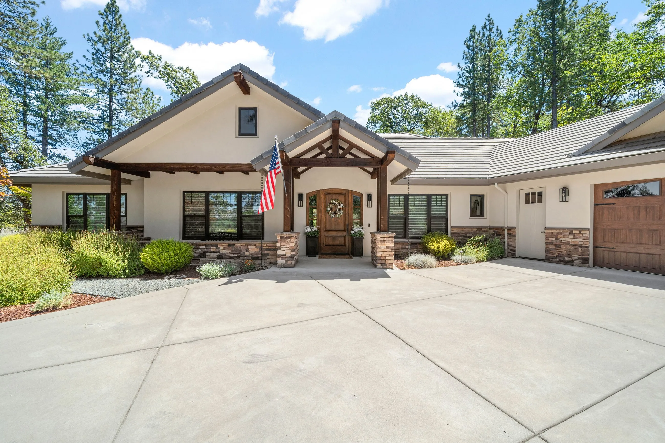 Timber-truss entry portico on stacked-stone columns with an arched knotty alder front door