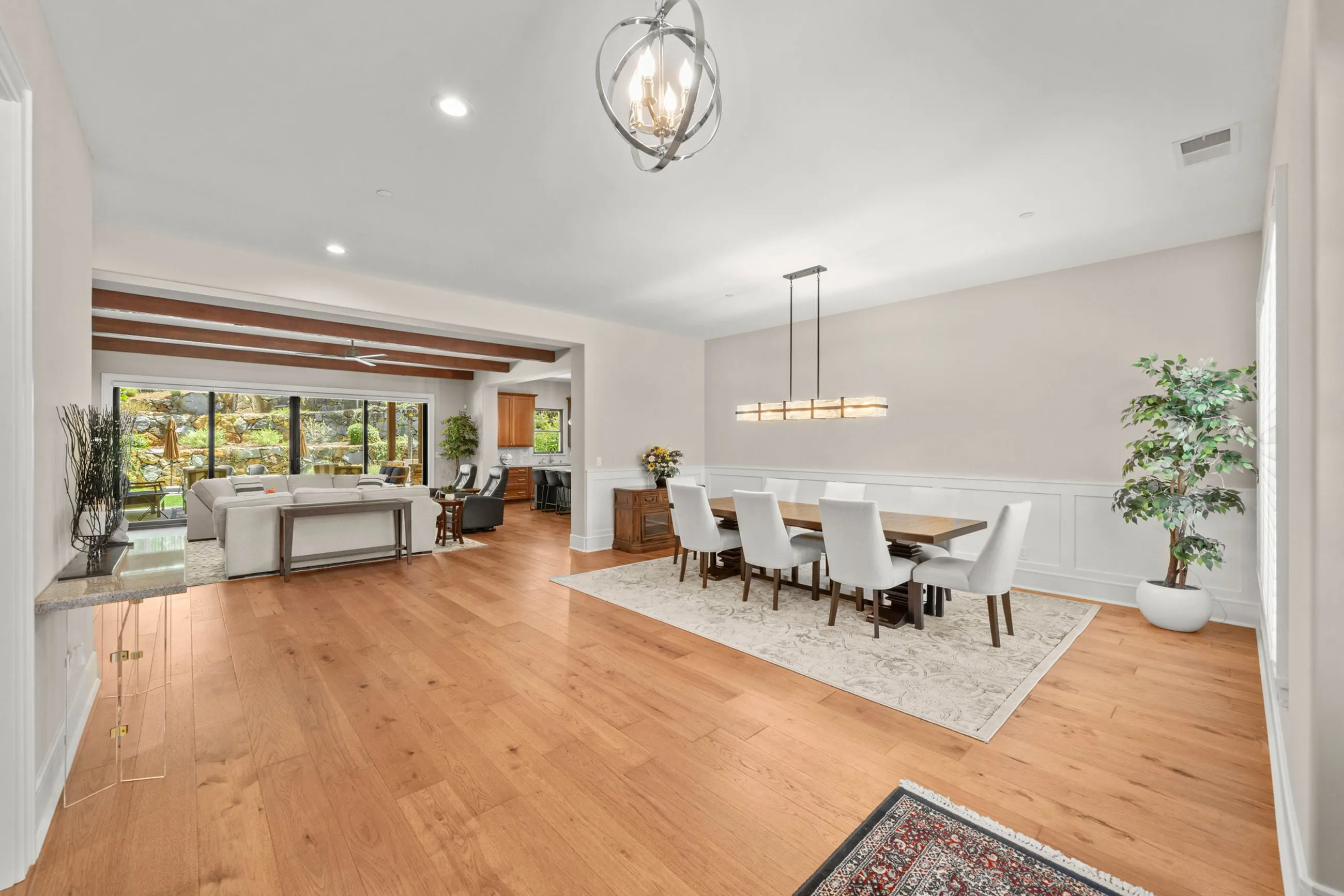 Open dining and living area with an orb chandelier, wainscoting, and wide-plank oak floors