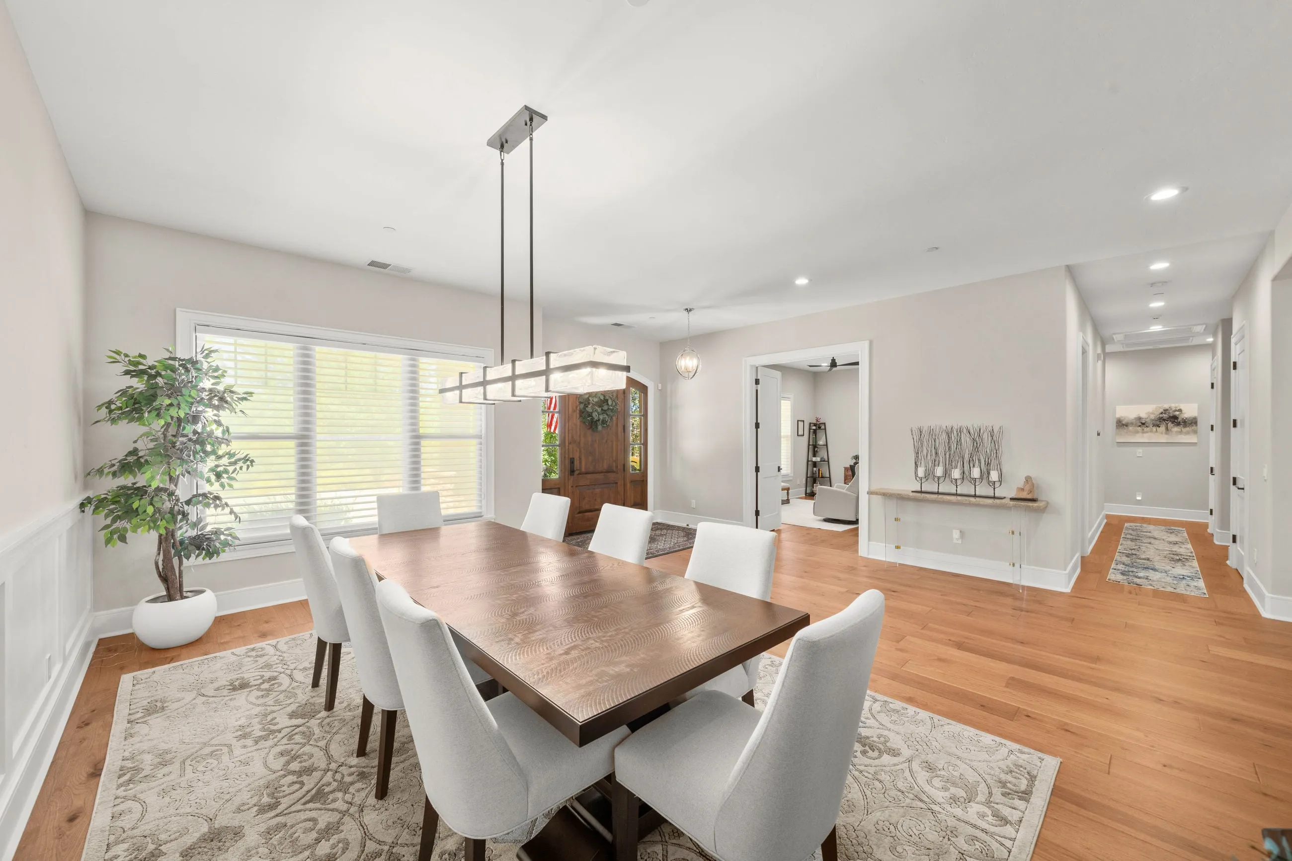 Dining room with a linear pendant, a wide window, and the arched alder entry door beyond