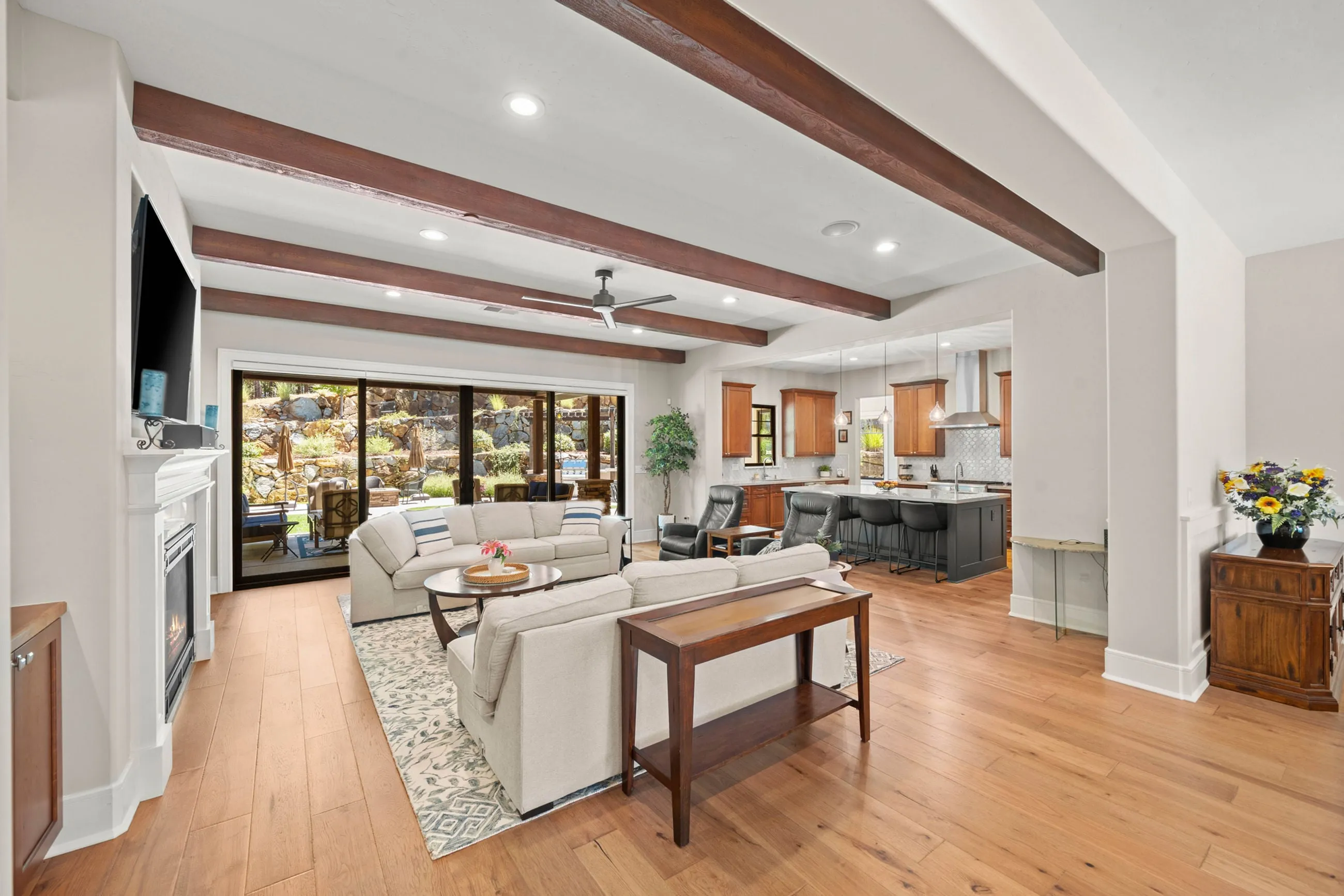 Great room with dark ceiling beams, white fireplace, and sliders opening to the covered patio