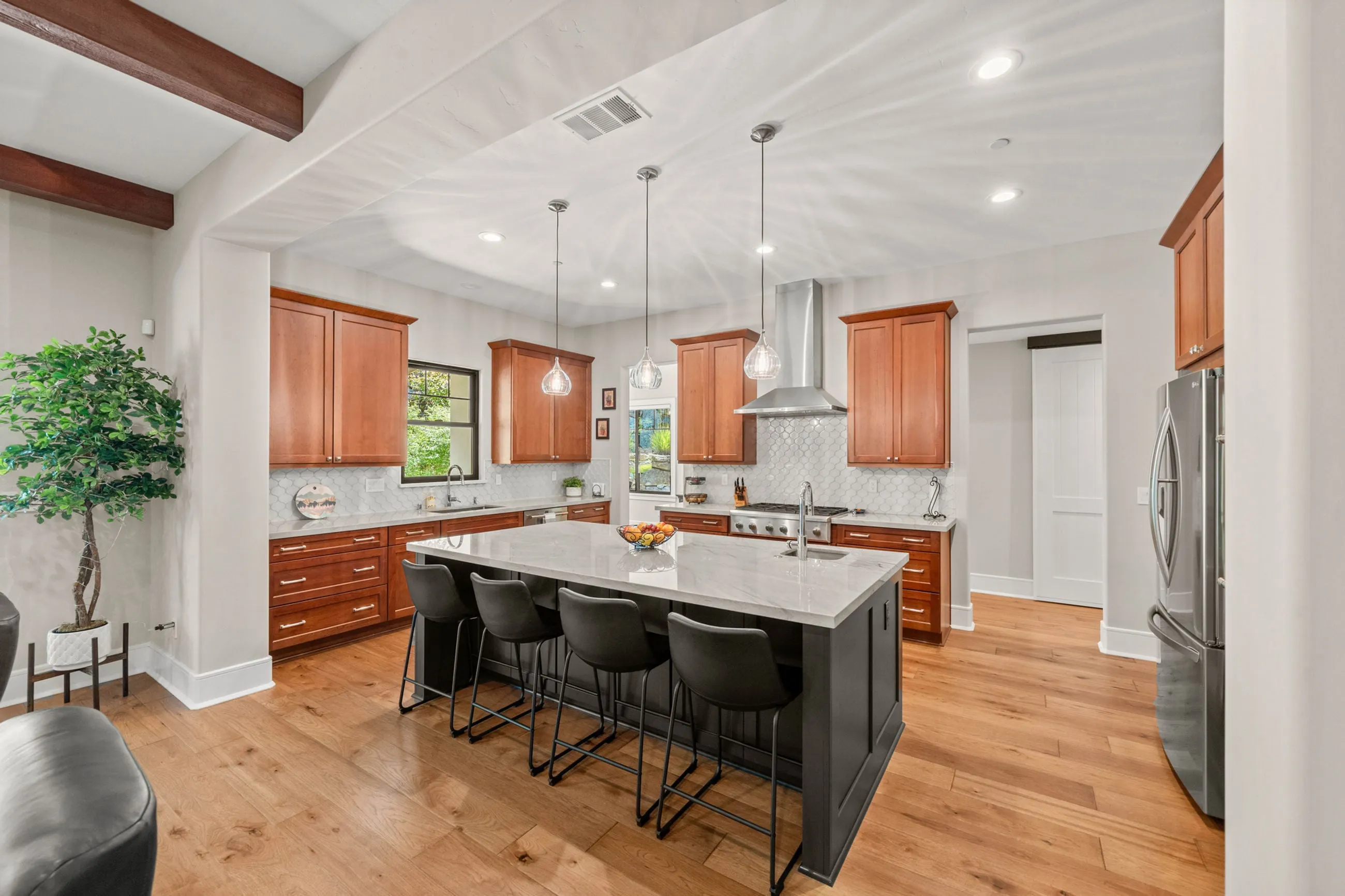 Kitchen with cherry cabinets, a black island seating four, quartz counters, and a stainless chimney hood