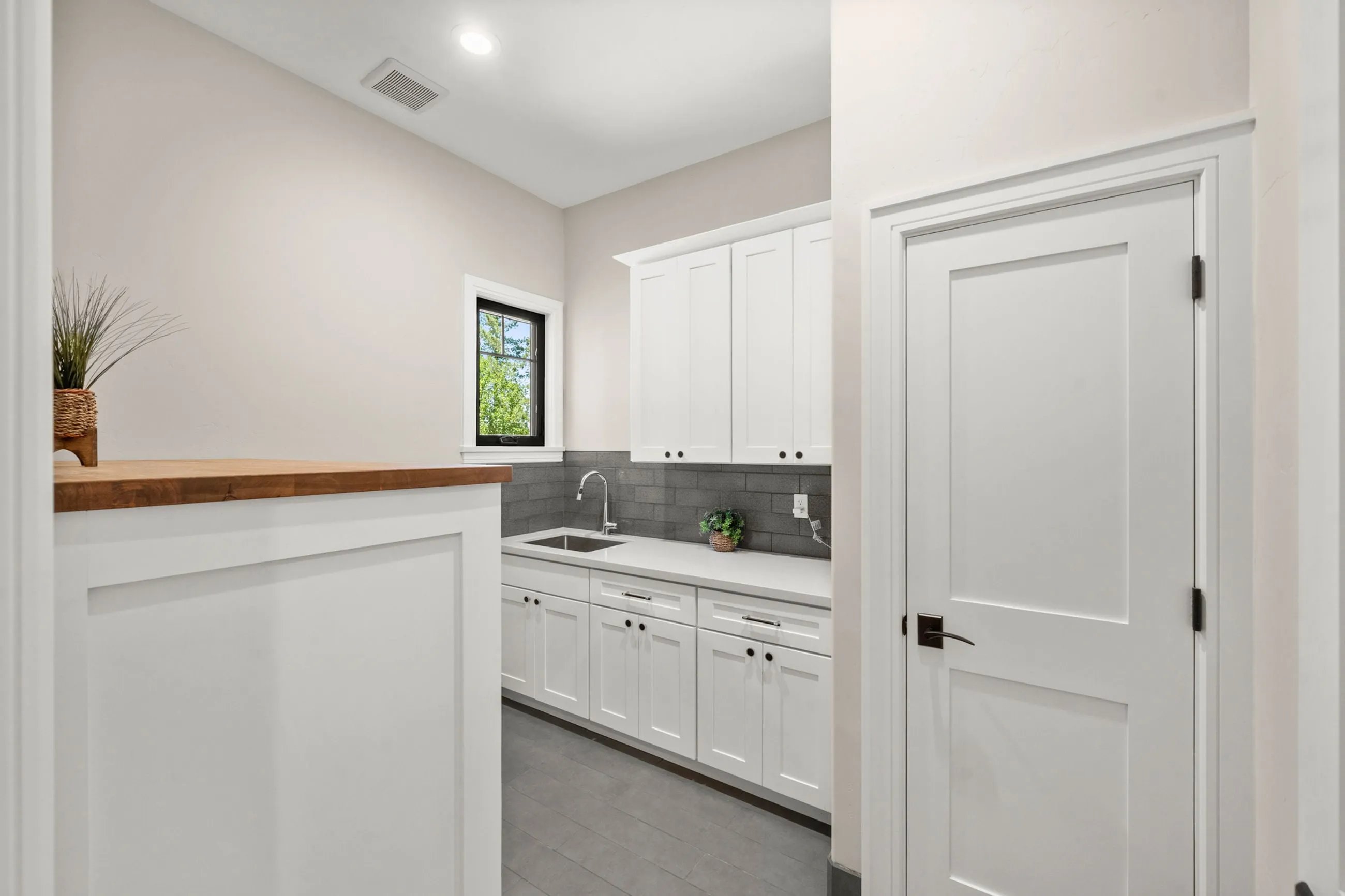Laundry room with white shaker cabinets, gray subway tile, and a butcher-block folding counter