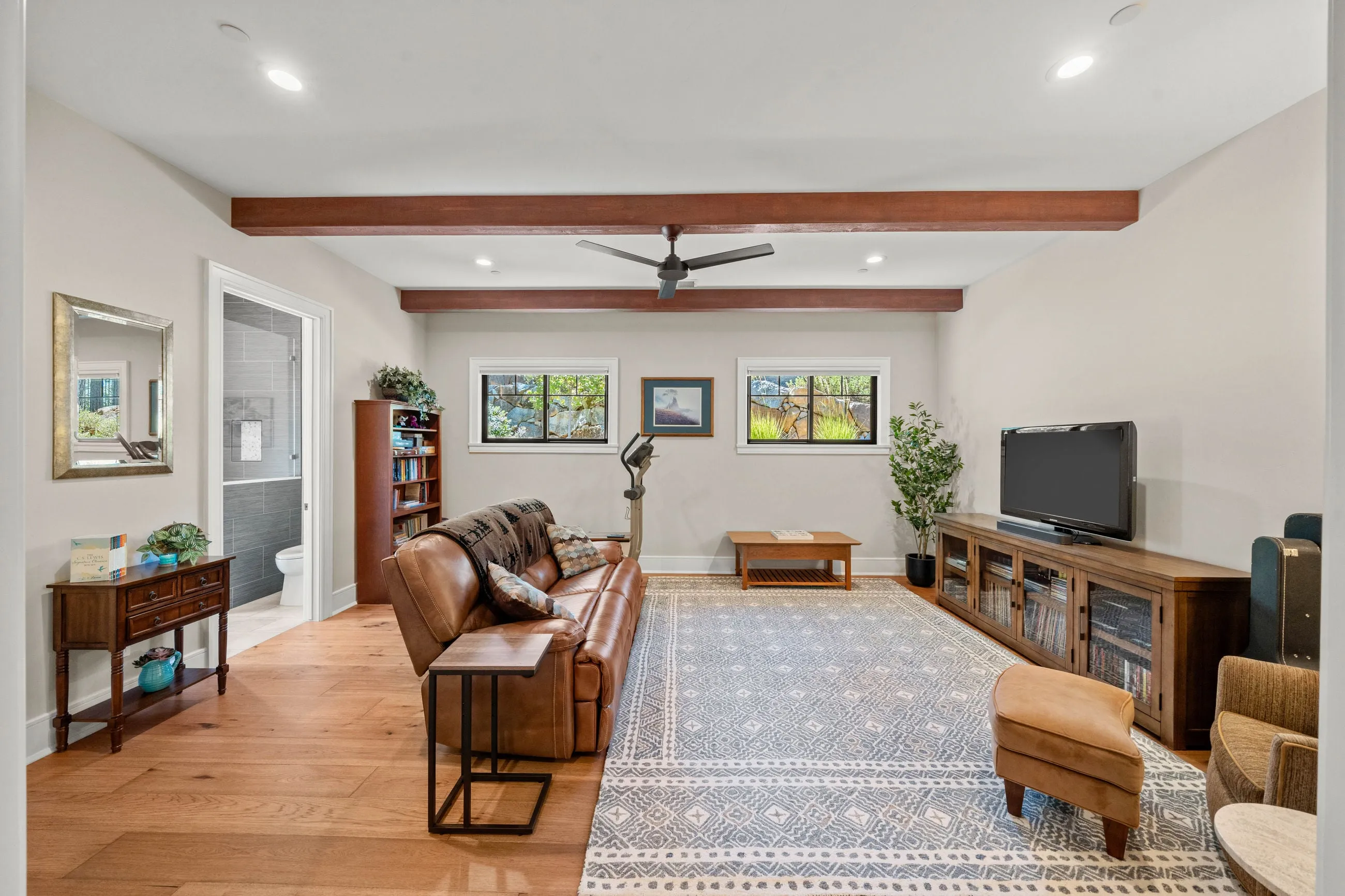 Family room with beamed ceiling, leather sofa, and a tiled ensuite bath through the doorway
