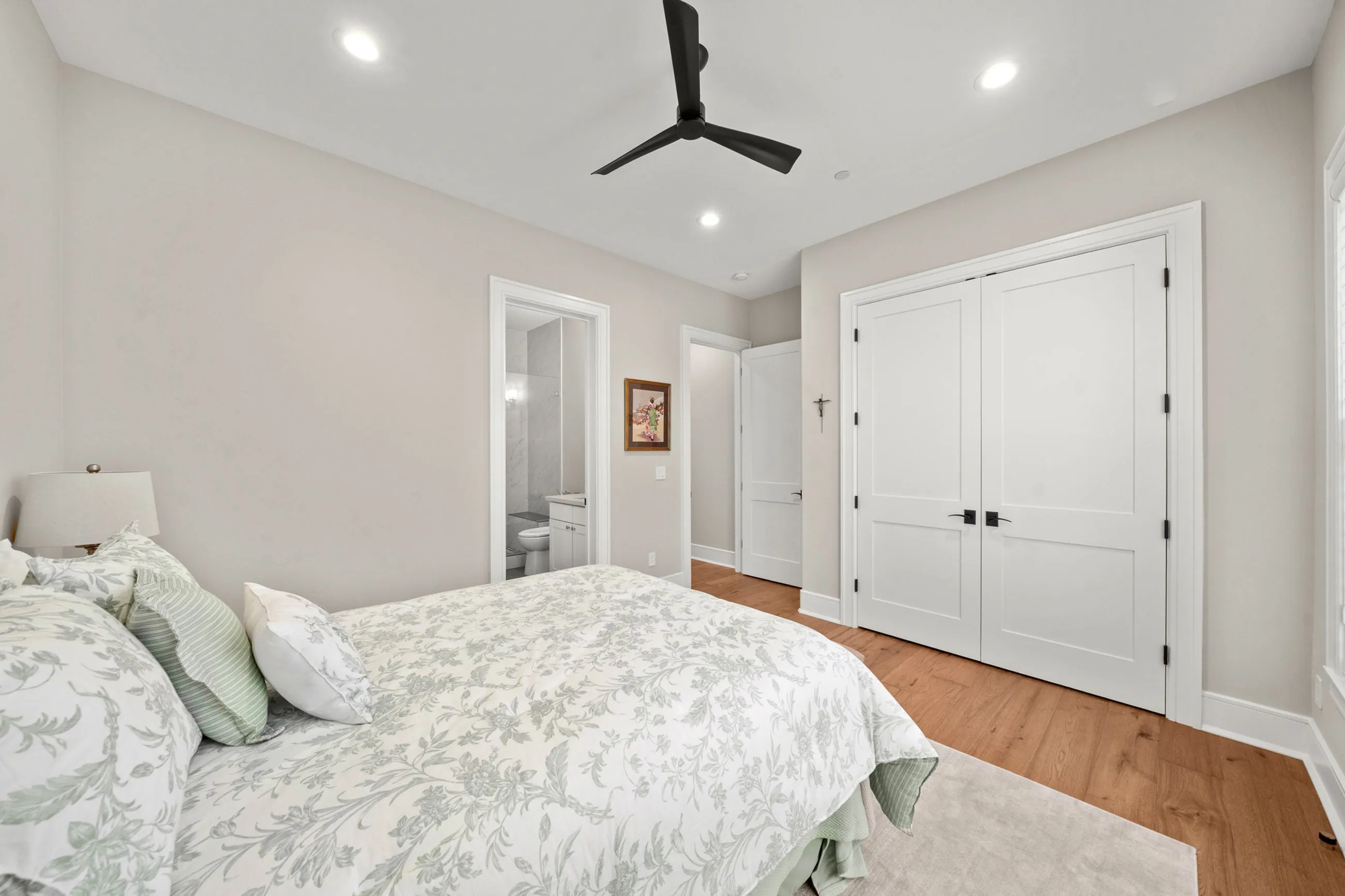 Second guest bedroom with ceiling fan, white double closet doors, and bath beyond