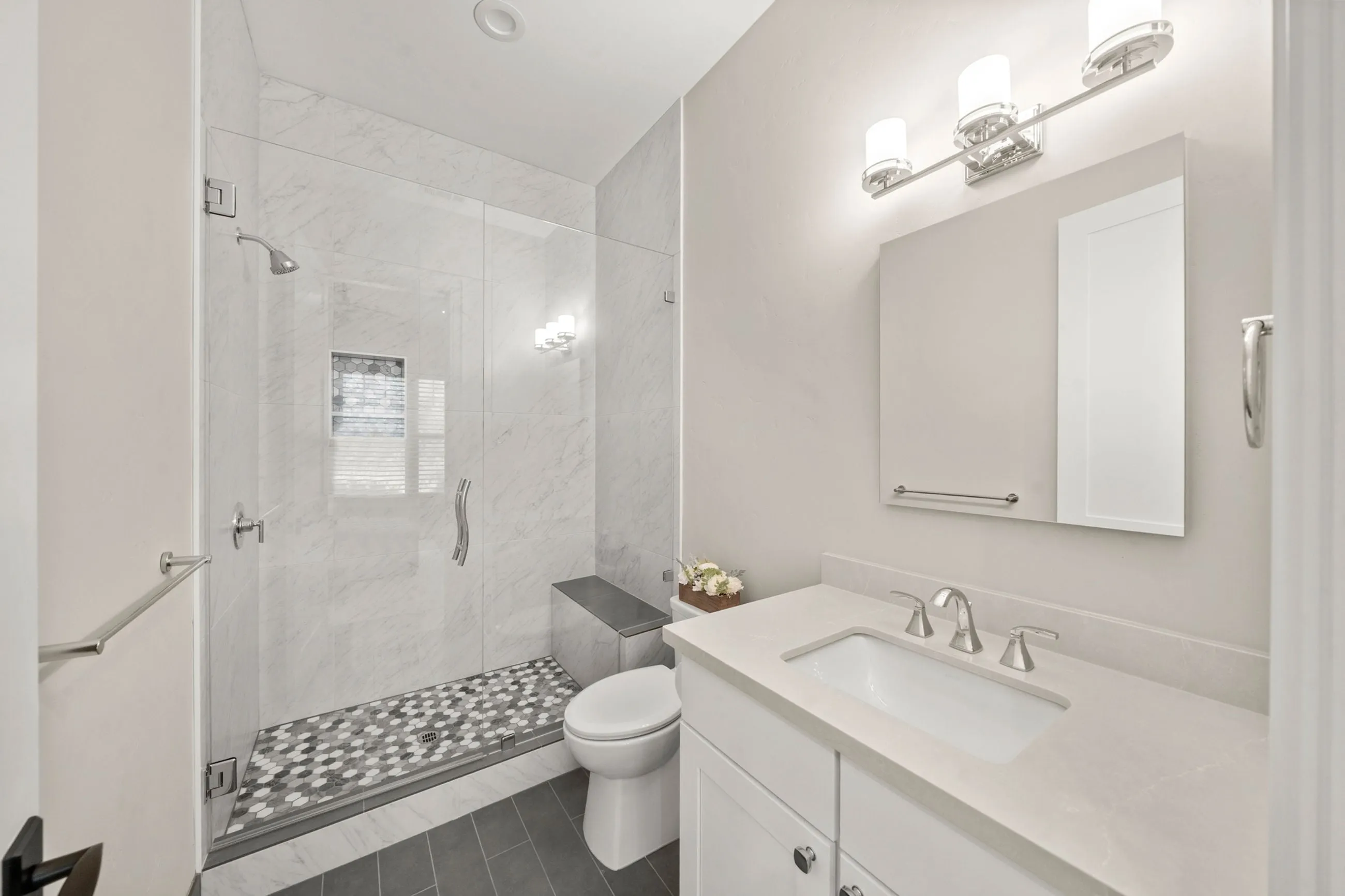 Guest bath with a glass-enclosed marble shower, penny-tile floor, and white vanity