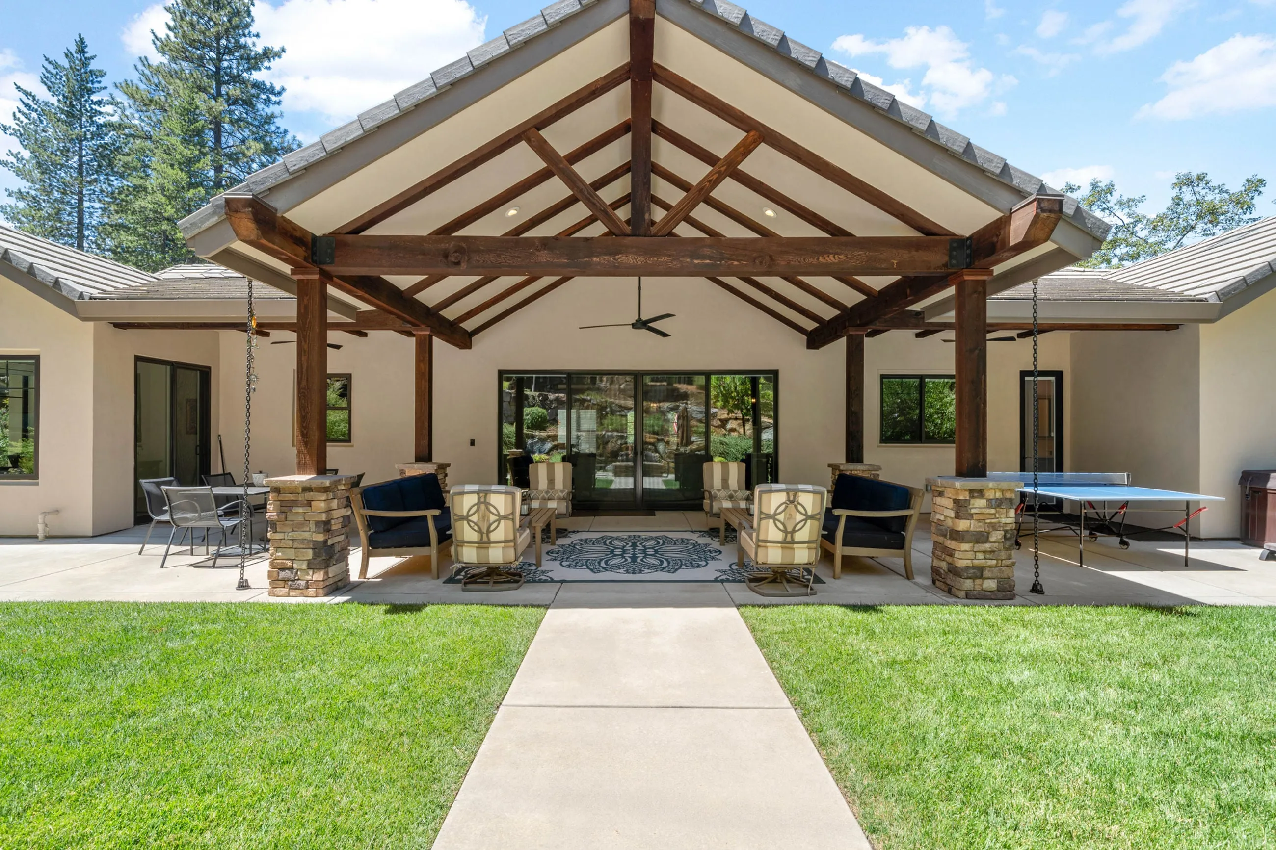 Rear elevation with the gabled timber-truss pavilion, ping-pong table, and concrete lawn path