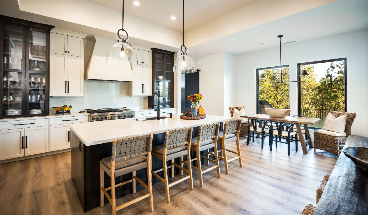 Kitchen island with woven-back barstools, glass pendants, and a sunny dining nook by the windows