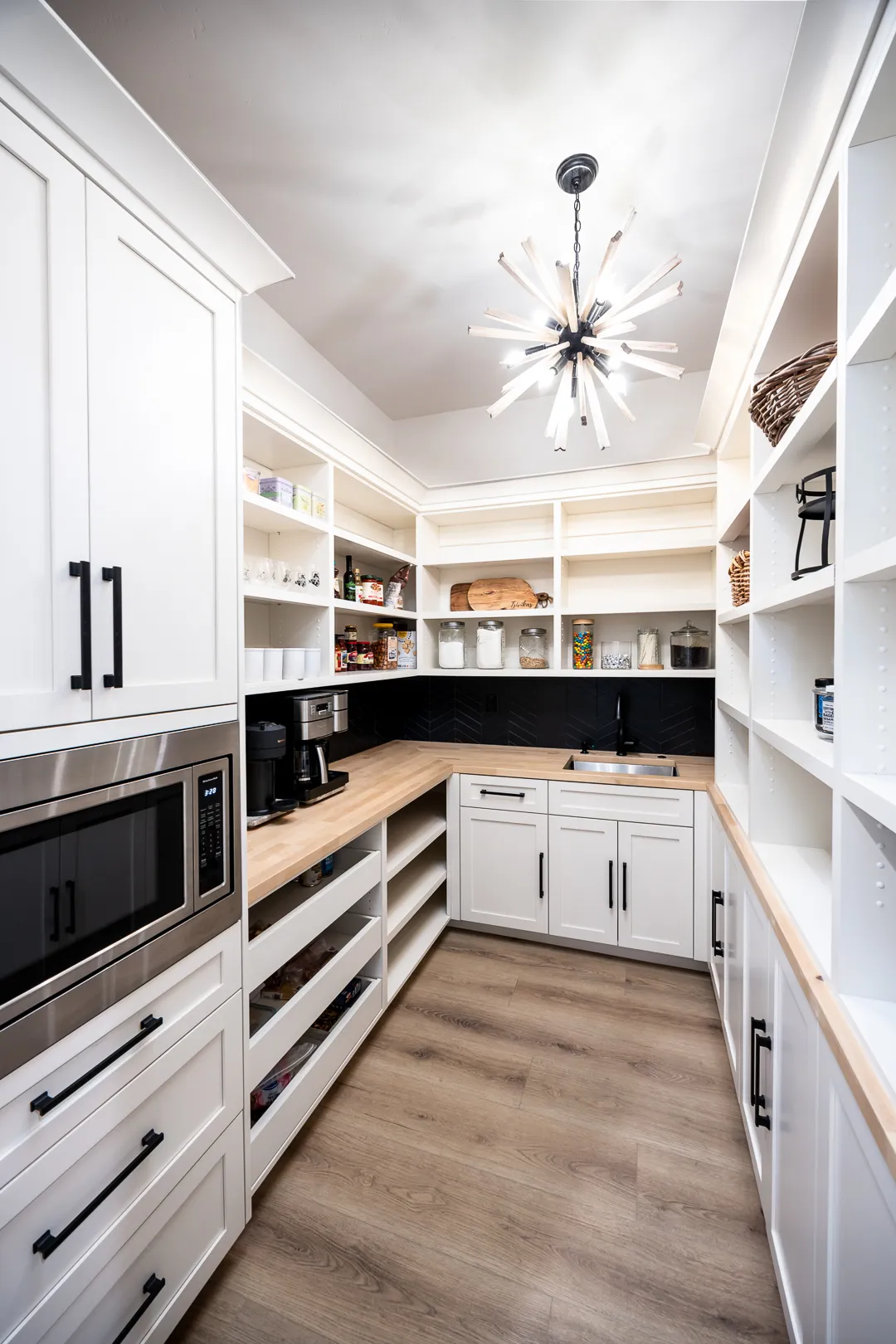 Walk-in pantry with butcher-block counters, black chevron tile backsplash, prep sink, and sputnik chandelier