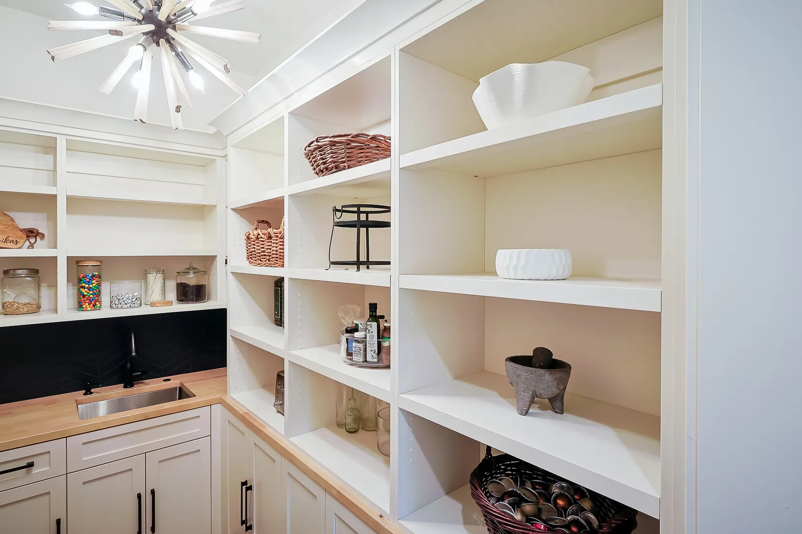 Pantry shelving detail with baskets, jars, and a wood-spoke sputnik light fixture overhead