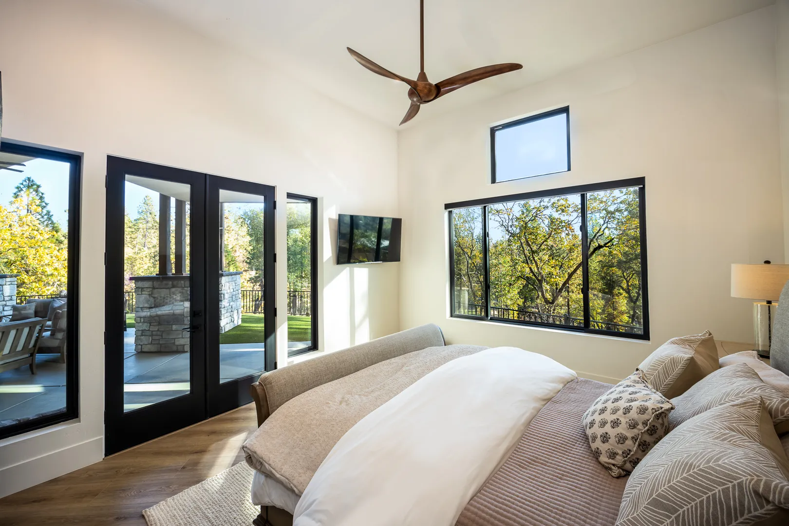 Primary bedroom with black-framed French doors opening to the covered patio and forest views