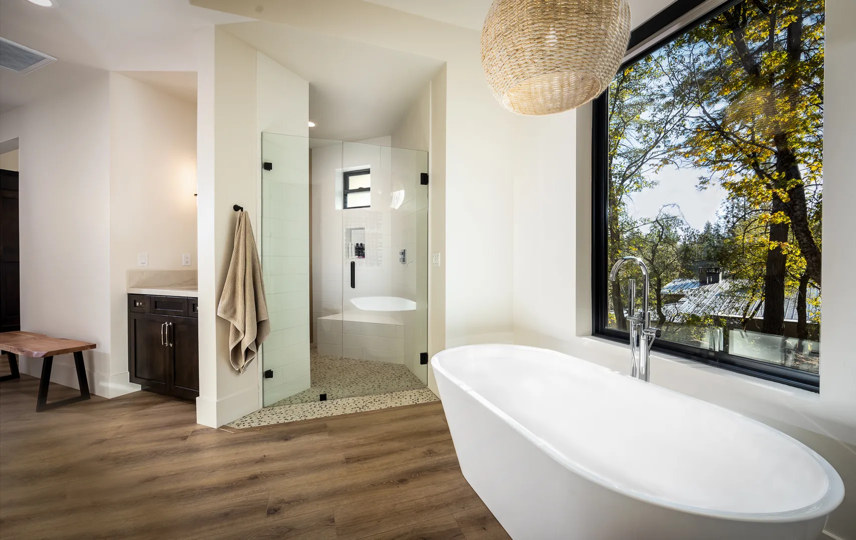 Primary bath with freestanding soaking tub beneath a picture window and walk-in glass shower