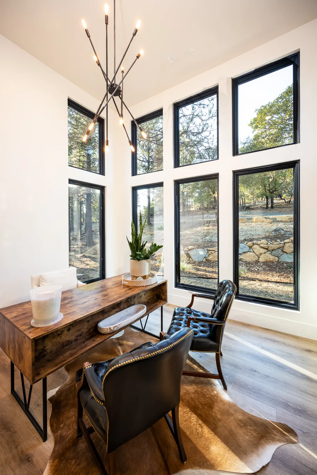 Two-story wall of black-framed windows in a home office with rustic desk and leather chairs