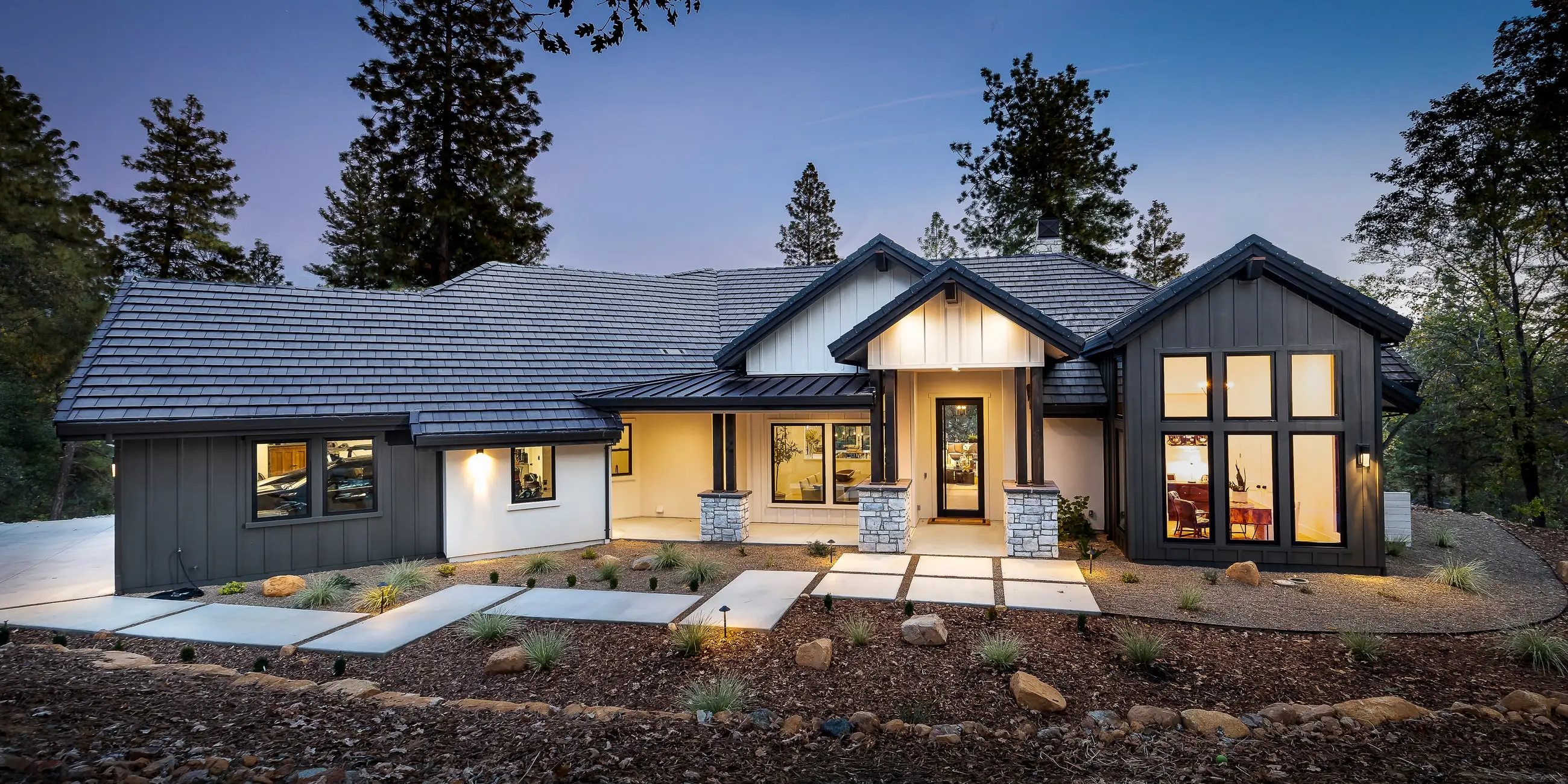 Front elevation of the Woodsy Elegance custom home at dusk, board-and-batten and stone among the pines in the Winchester Country Club