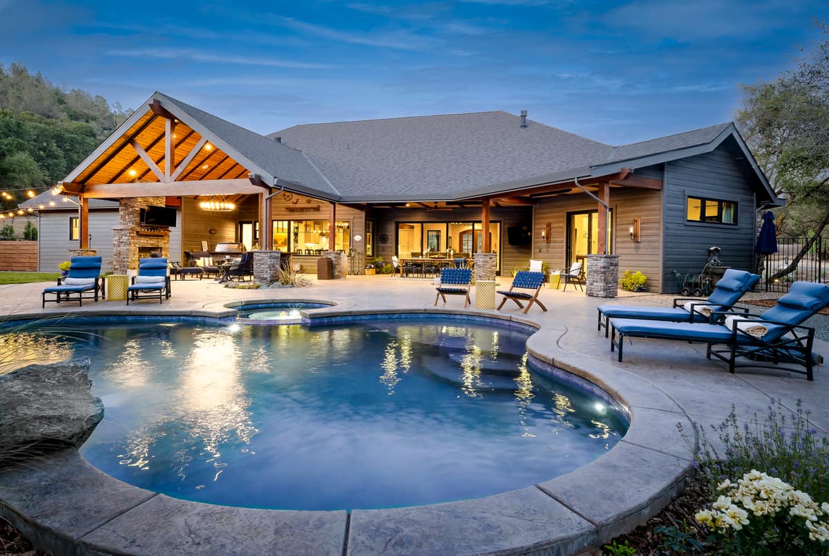 Custom home at dusk with a timber-truss outdoor pavilion, stone columns and a lit pool in the Sierra foothills