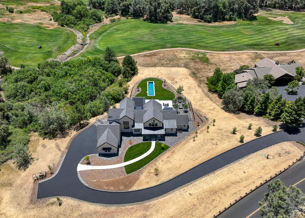 Drone view of a new custom home, detached garage, lap pool and long driveway on a golf-course lot in the Placer County foothills
