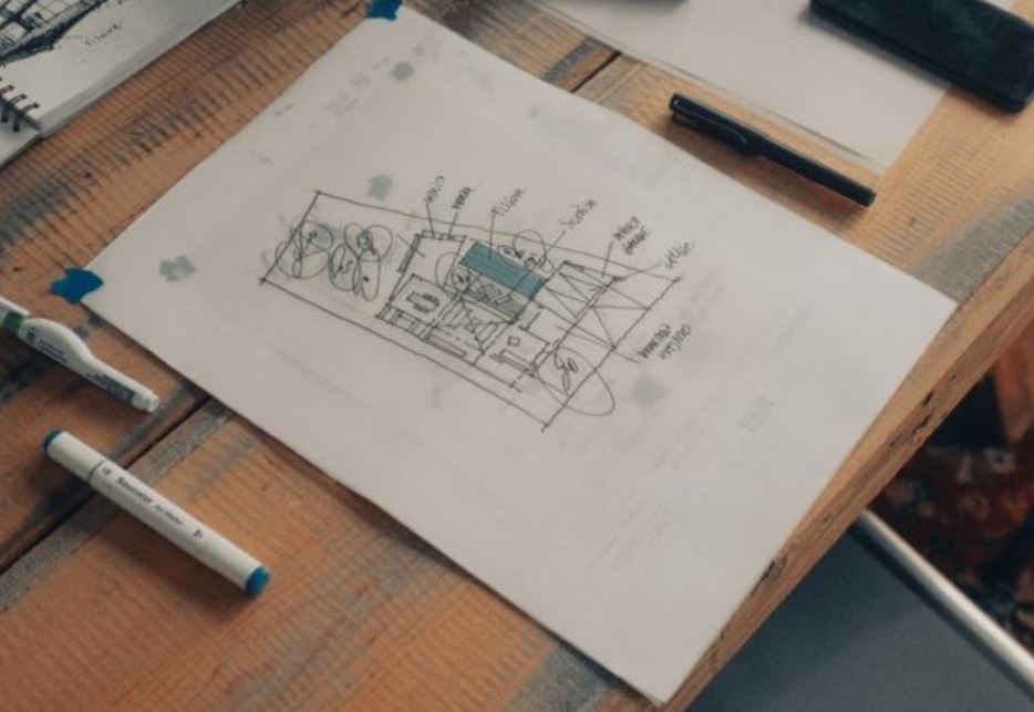 Hand-sketched floor plan taped to a wooden desk beside markers and a pen