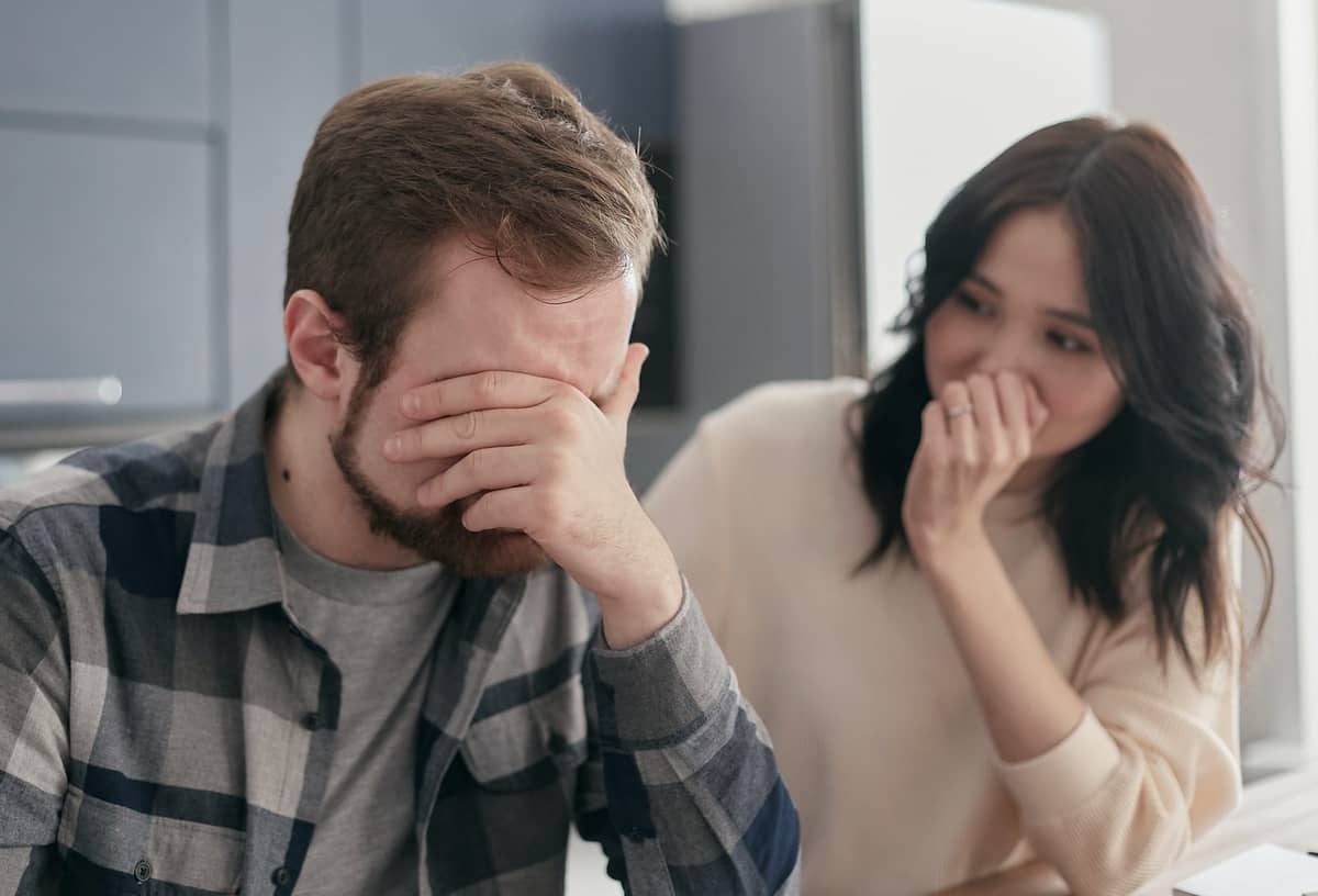 A worried couple in a kitchen, the man with his hand over his face after a construction cost surprise