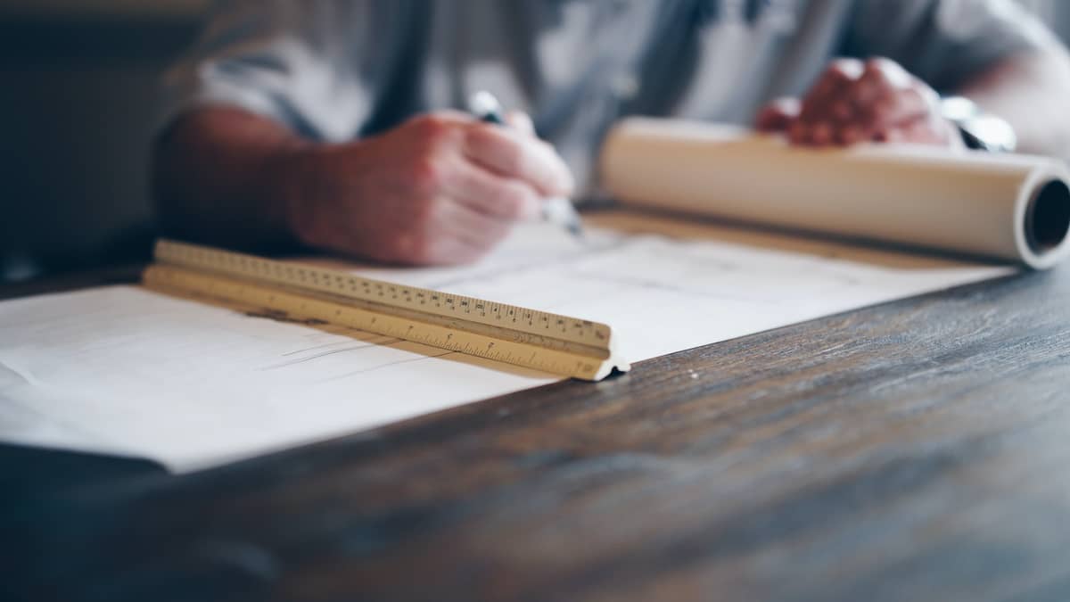 Architect working on rolled building plans with a triangular scale ruler in the foreground