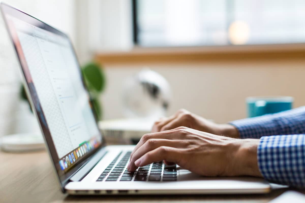 Hands typing on a laptop keyboard at a desk near a bright window