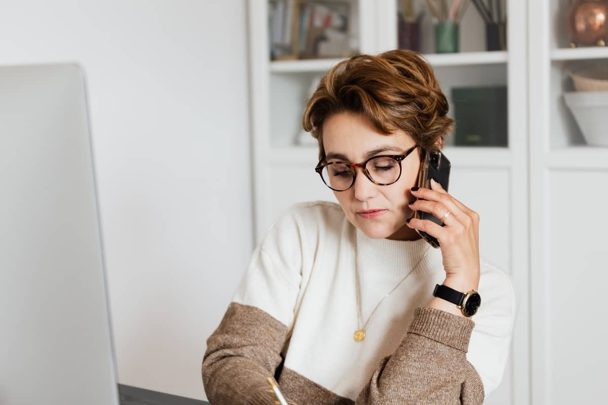 Woman in glasses taking a phone call at her desk in a home office