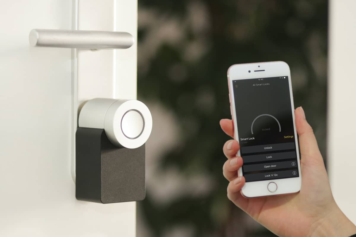 A hand holding a smartphone to unlock a keyless smart lock on a white front door