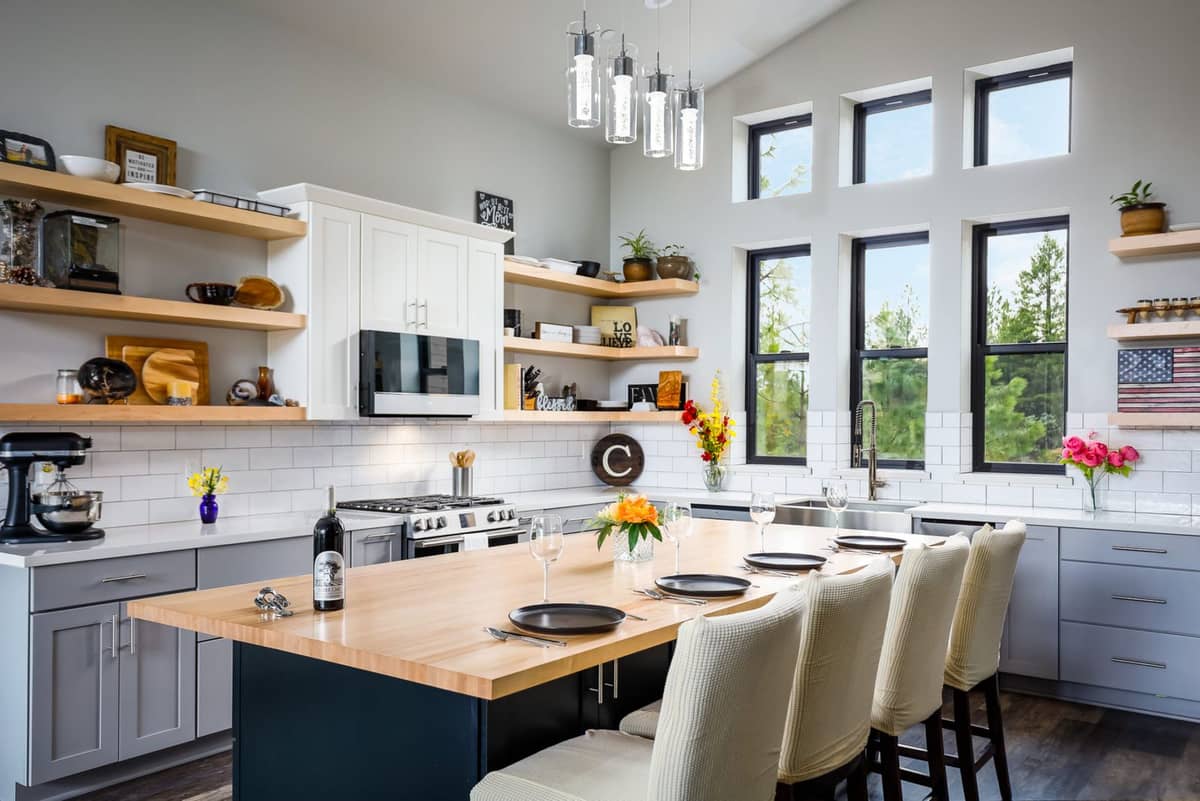 Bright kitchen with tall windows, open wood shelving, and a butcher-block island set for dinner